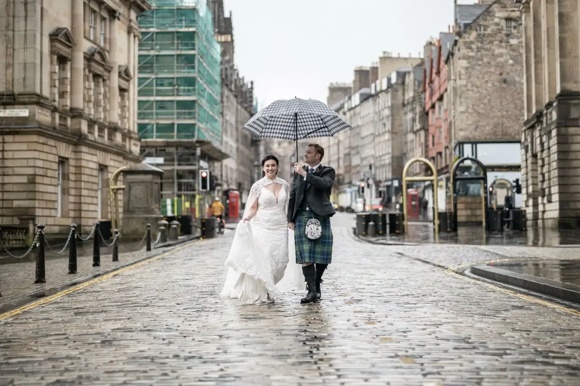 Newlyweds walking down the middle of the road on the Royal Mile in the rain
