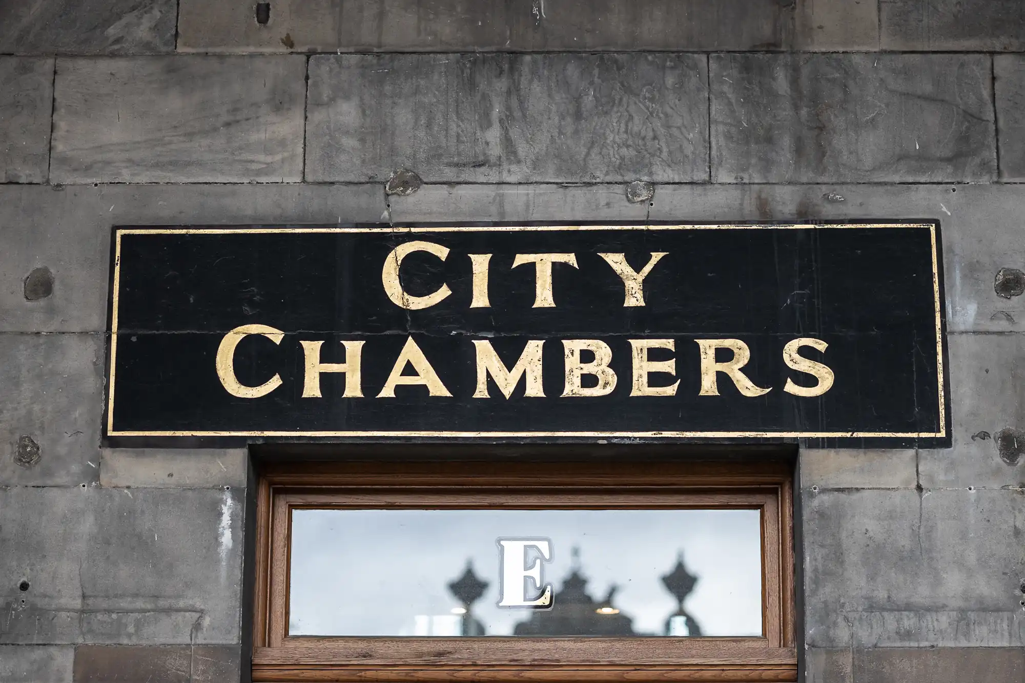 A black sign with gold letters reading "CITY CHAMBERS" is mounted on a stone wall above a window.