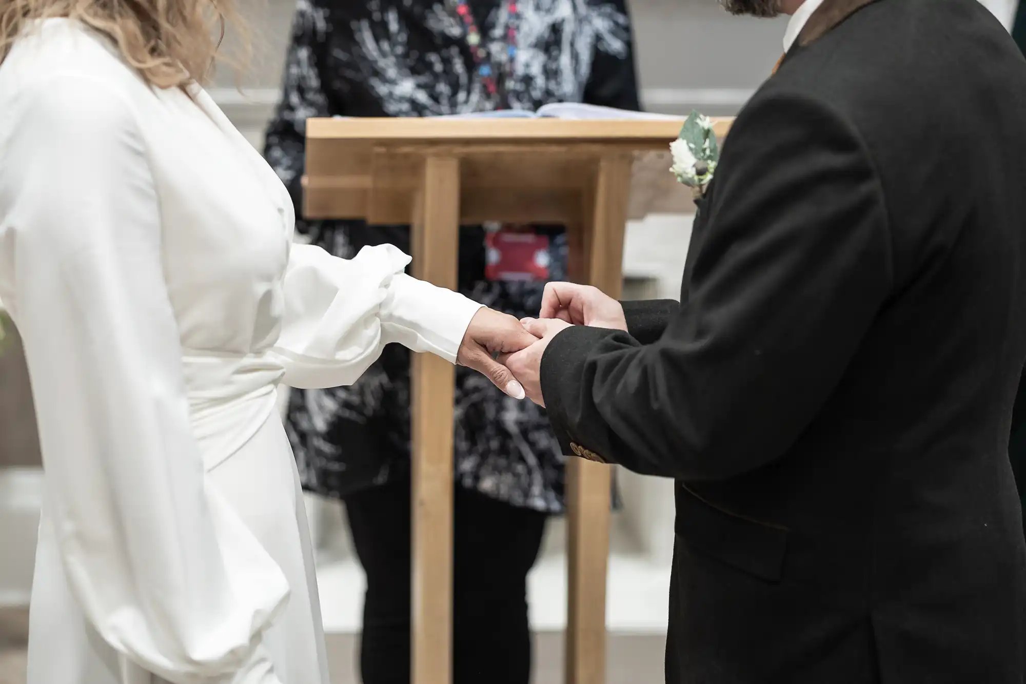 A man and woman stand facing each other and holding hands in front of a lectern, with an individual standing behind it.