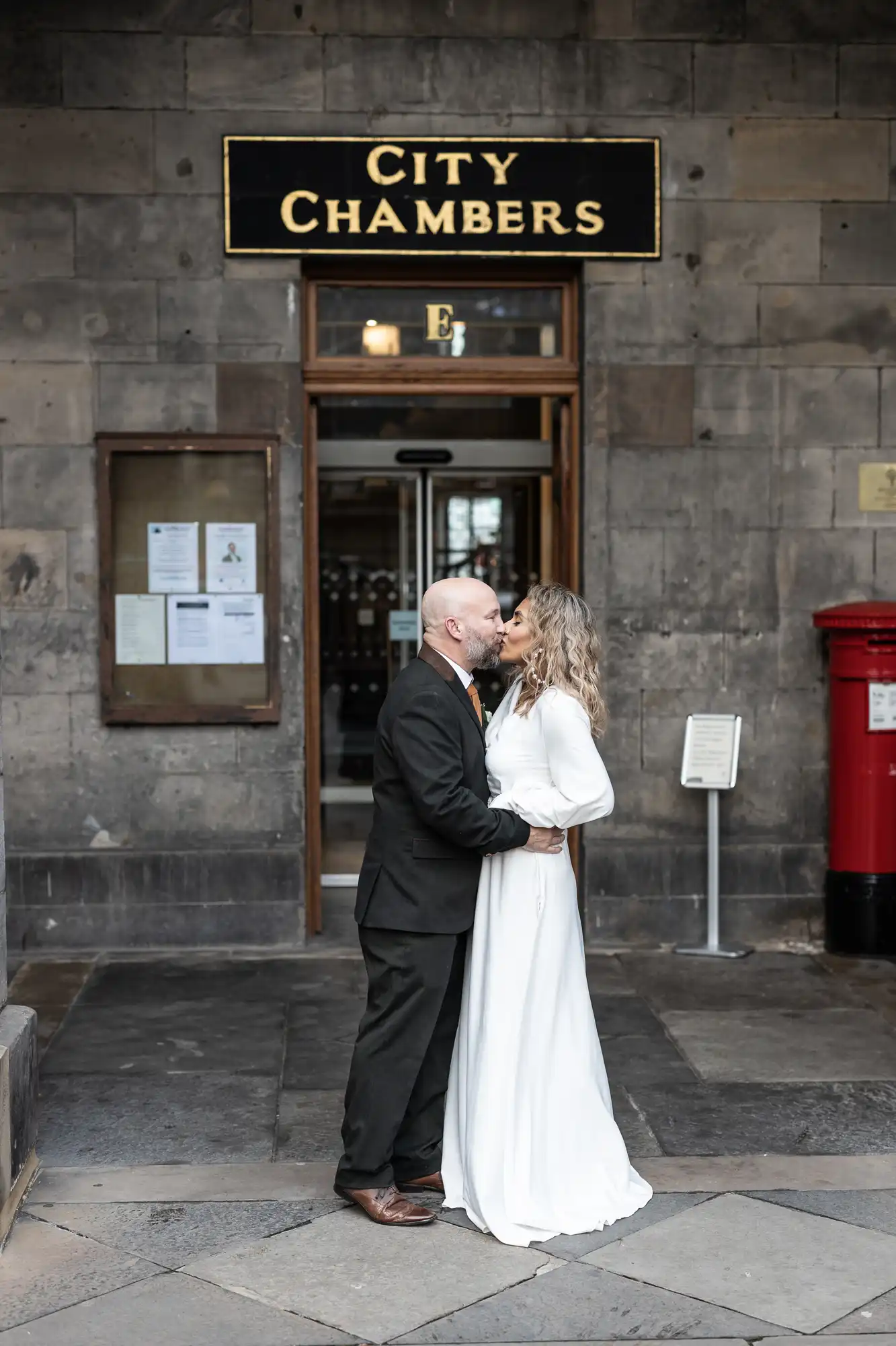 A couple in wedding attire shares a kiss in front of City Chambers.