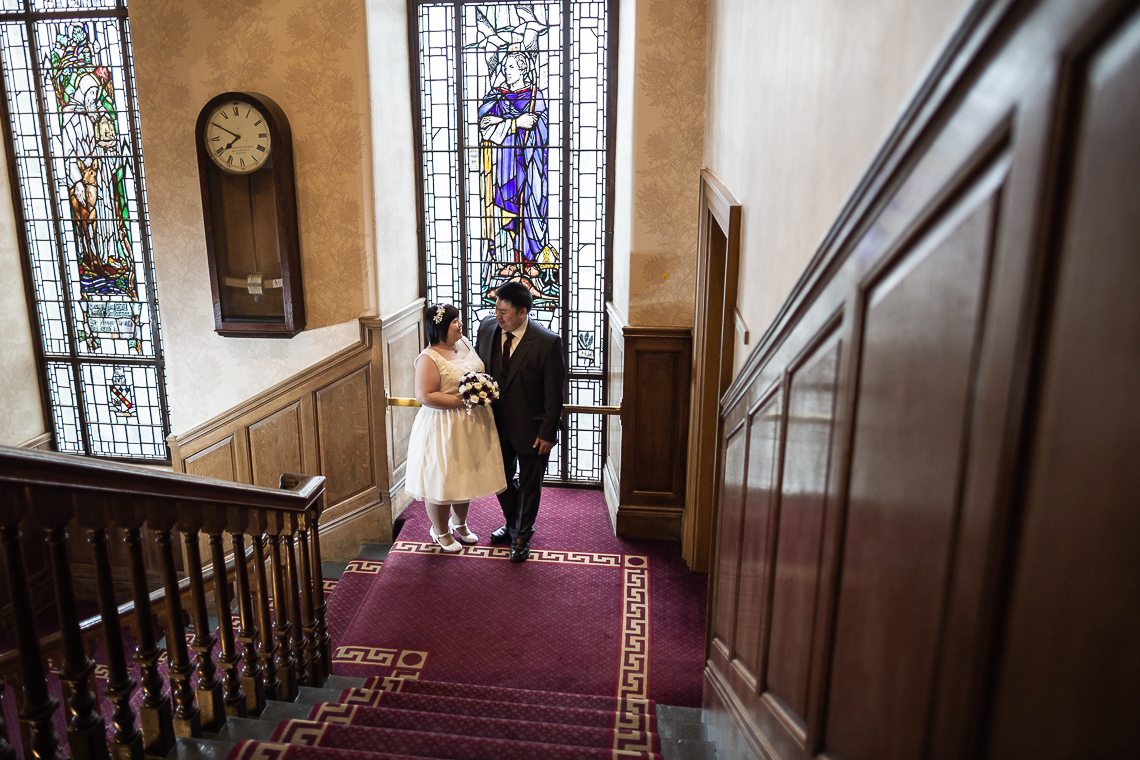 newlyweds standing in front of the stained glass window on the staircase