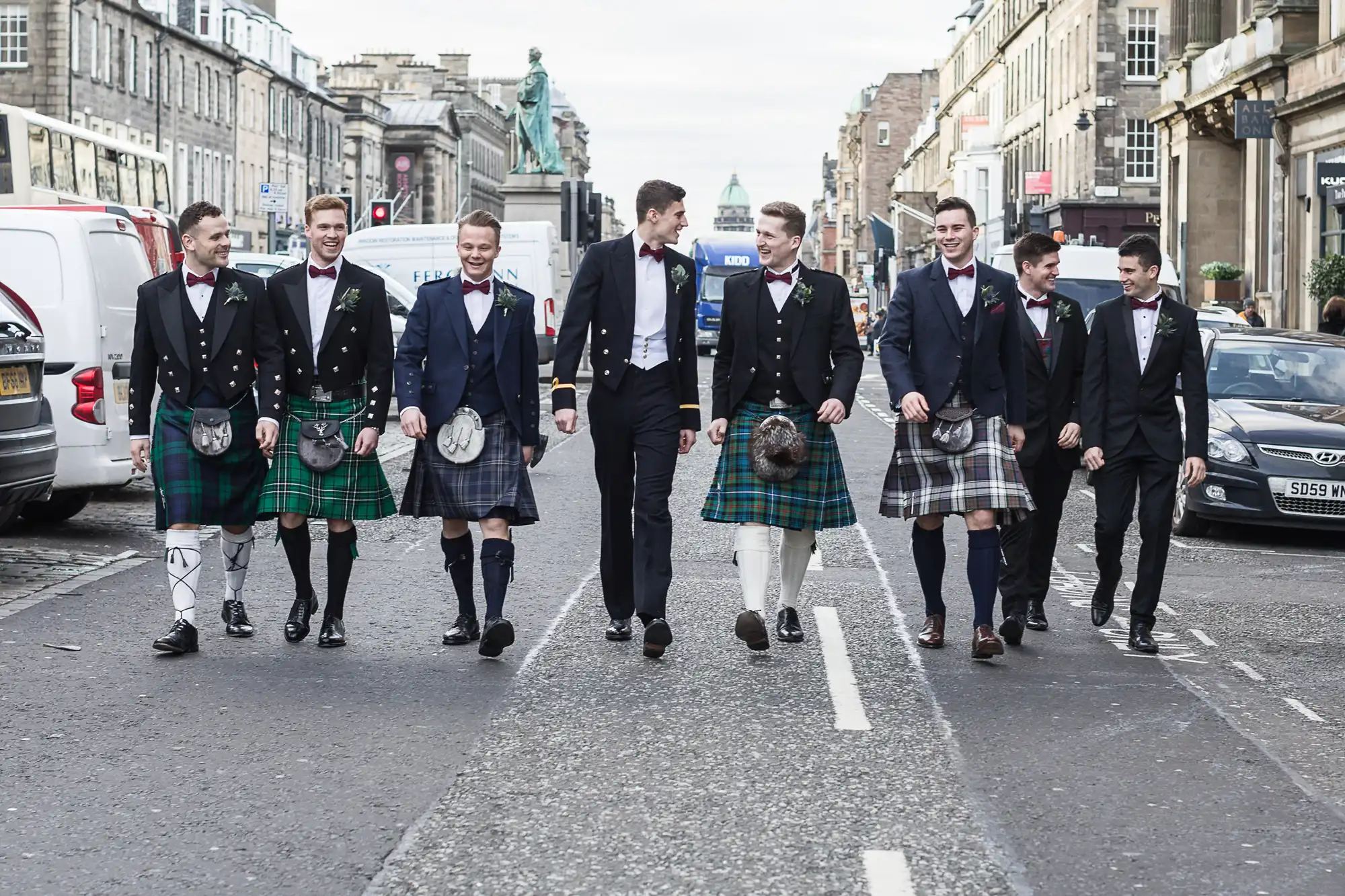 A group of men, some in kilts and some in suits, walk down a city street.