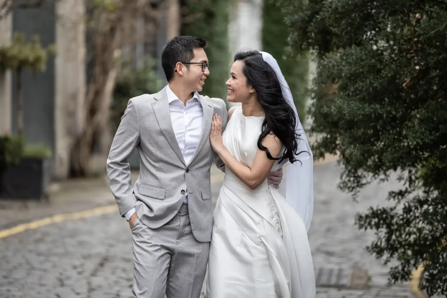 Best photo locations in Edinburgh for couples - photography tips by Love Wedding Photos and Film. Edinburgh's most Instagrammable locations featuring a couple, dressed in smart attire, smile and walk arm-in-arm on a cobblestone path lined with trees.