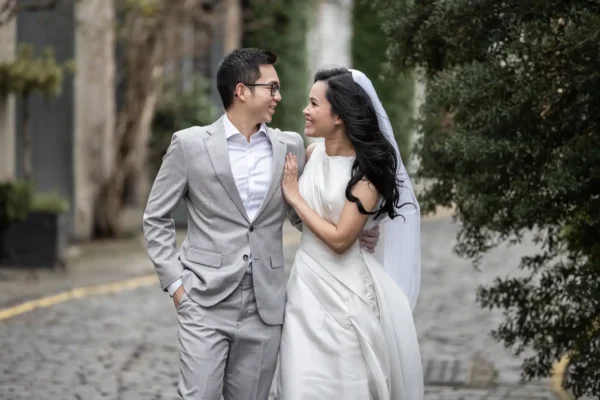 Best photo locations in Edinburgh for couples - photography tips by Love Wedding Photos and Film. Edinburgh's most Instagrammable locations featuring a couple, dressed in smart attire, smile and walk arm-in-arm on a cobblestone path lined with trees.