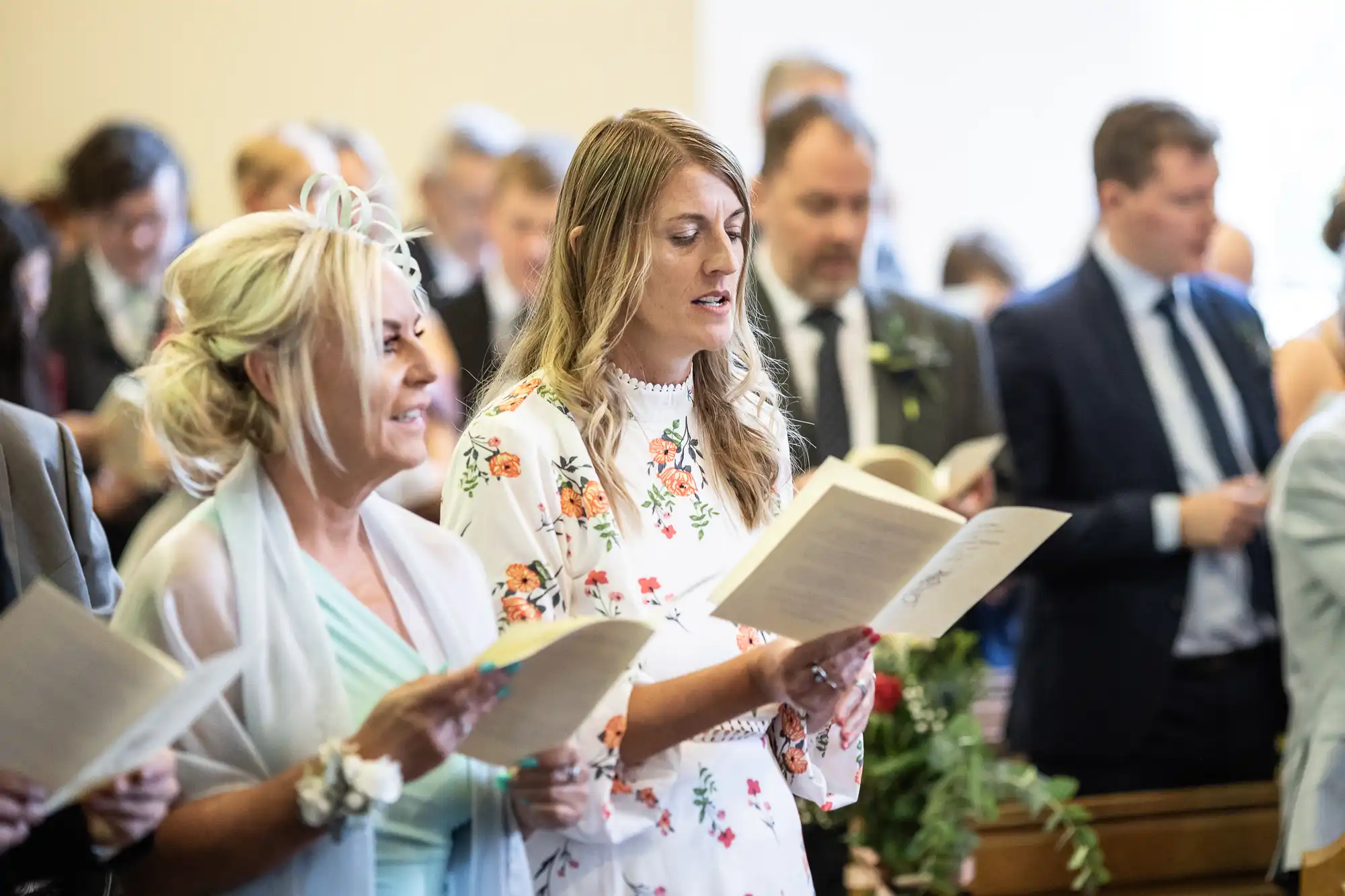 People standing in a church, holding and reading from hymn books during a service.