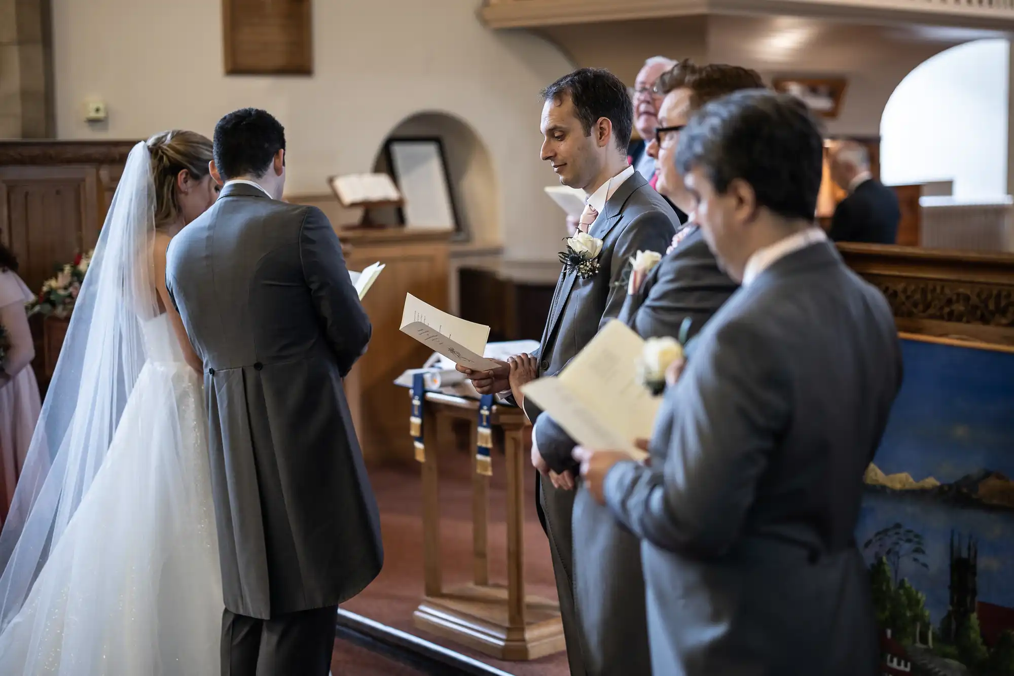 A bride and groom stand at the altar with groomsmen holding programs during a wedding ceremony in a church.