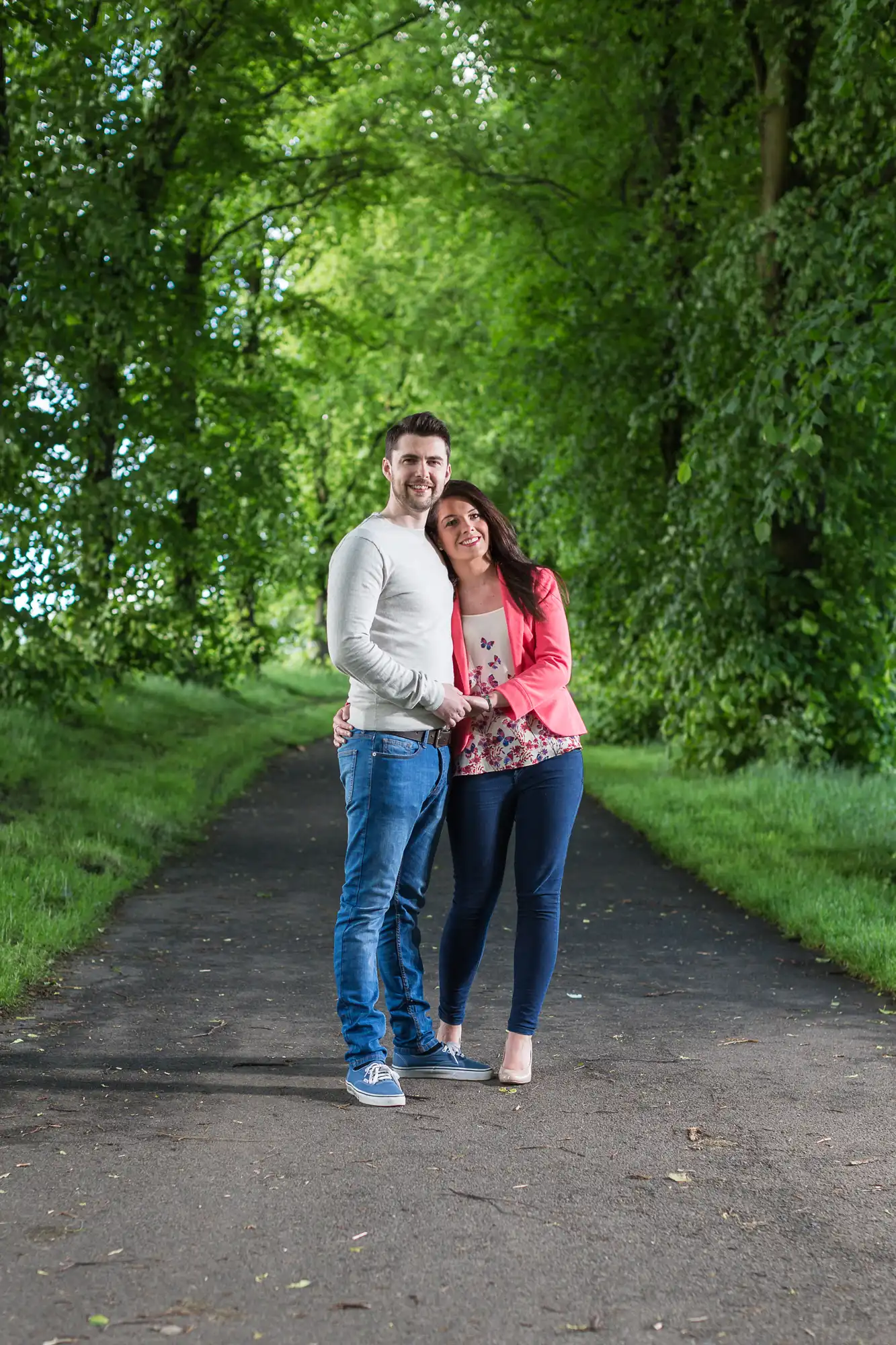 A couple embracing and smiling on a tree-lined path.