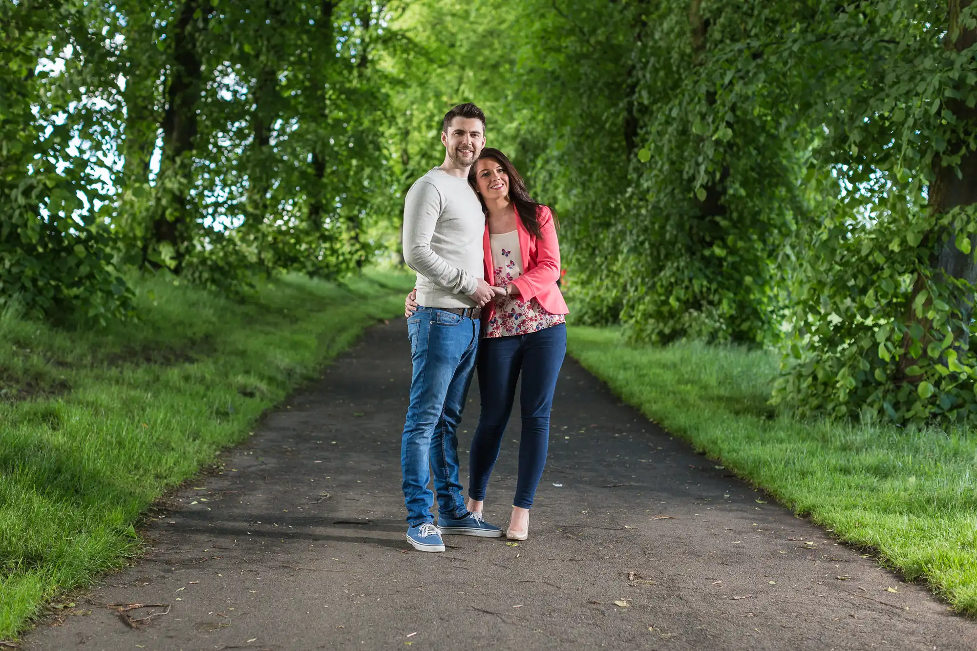 A happy couple embracing while standing on a tree-lined path in a park.