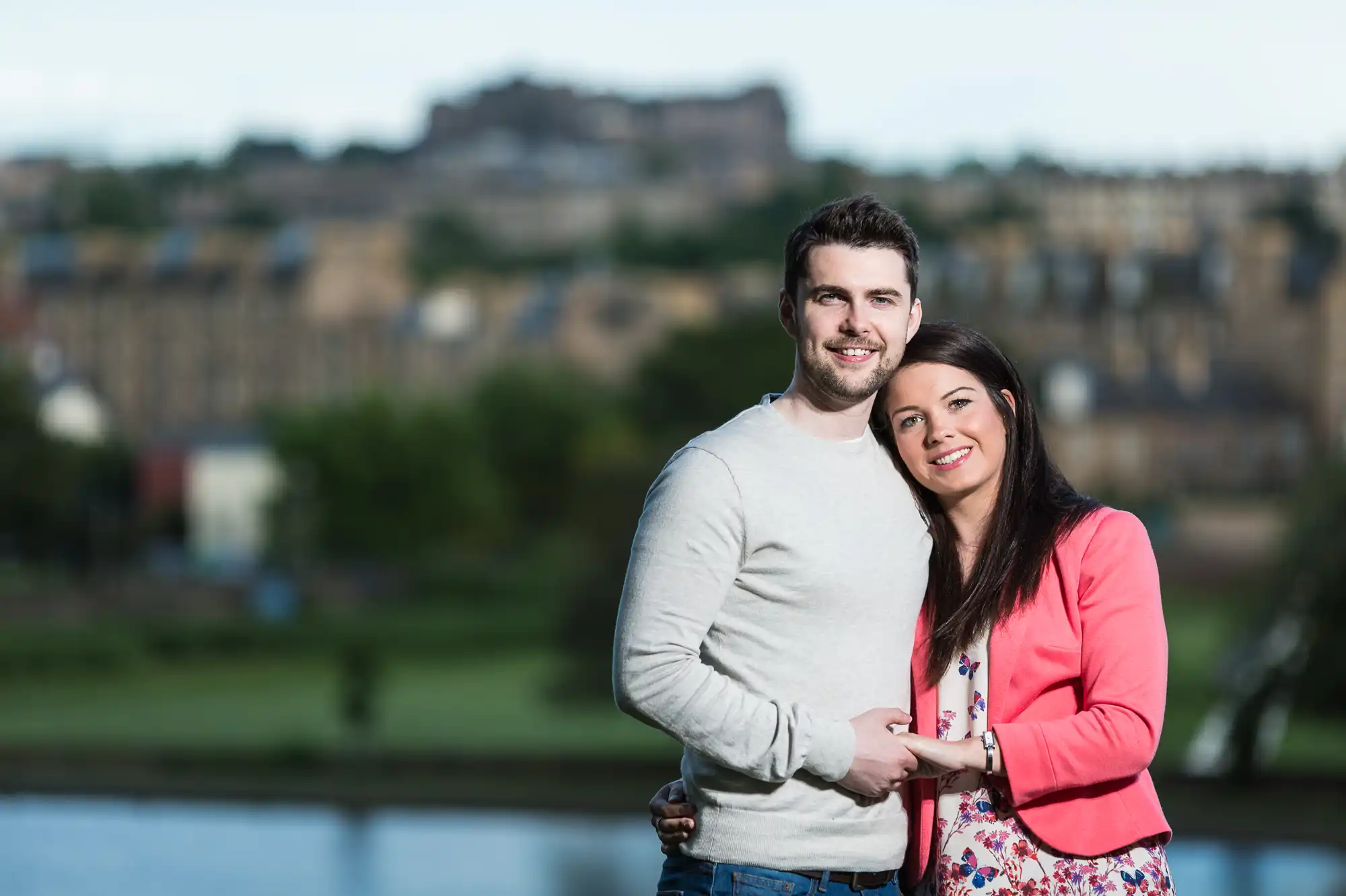 A couple smiling at the camera with a scenic cityscape and a castle in the background.
