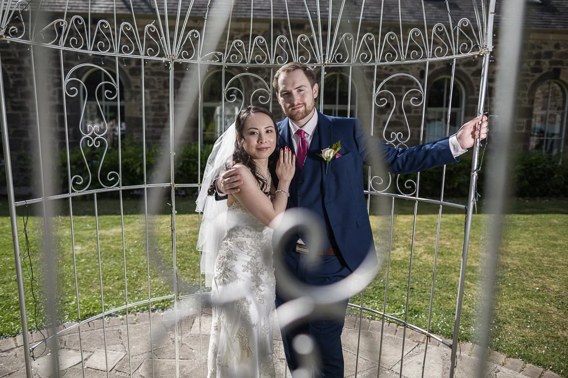 Newlyweds embrace inside the bird cage in the garden.