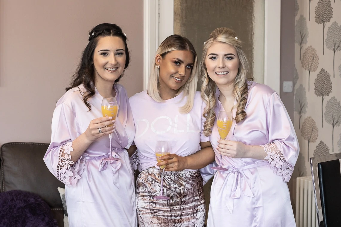 bridesmaids in dressing gowns and makeup artist Ava Spence with a glass of fizz