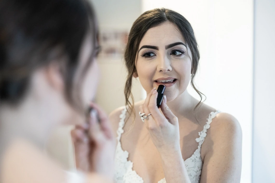bride looking in a mirror applying lipstick wearing Rosa Clara dress