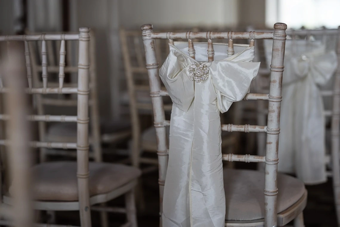 A wedding dress with embellished details hanging on a distressed wooden chair in a softly lit room.