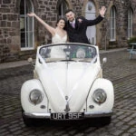 Eskmills Venue Wedding - Blythe and Dean standing waving in a convertible VW Beetle