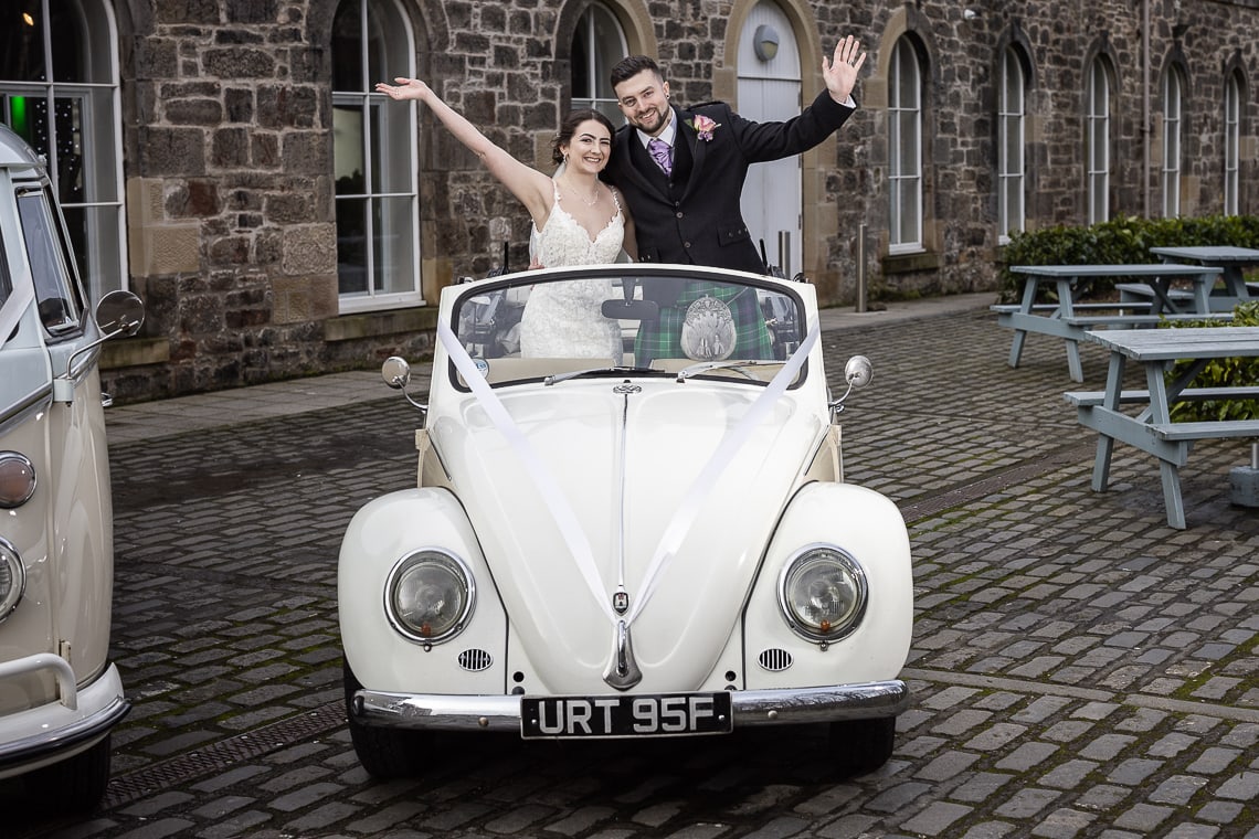 Eskmills Venue Wedding - Blythe and Dean standing waving in a convertible VW Beetle