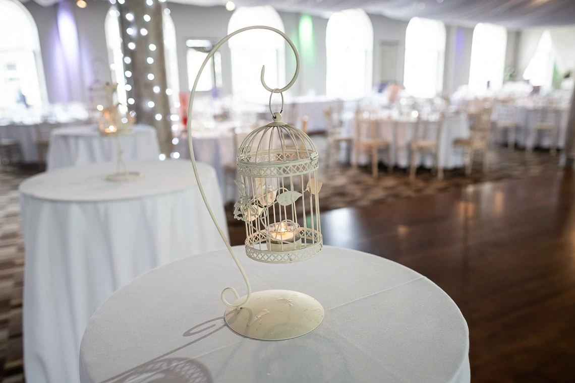 Decorative candle lantern on a table at a wedding reception, with elegantly set tables and string lights in the background.