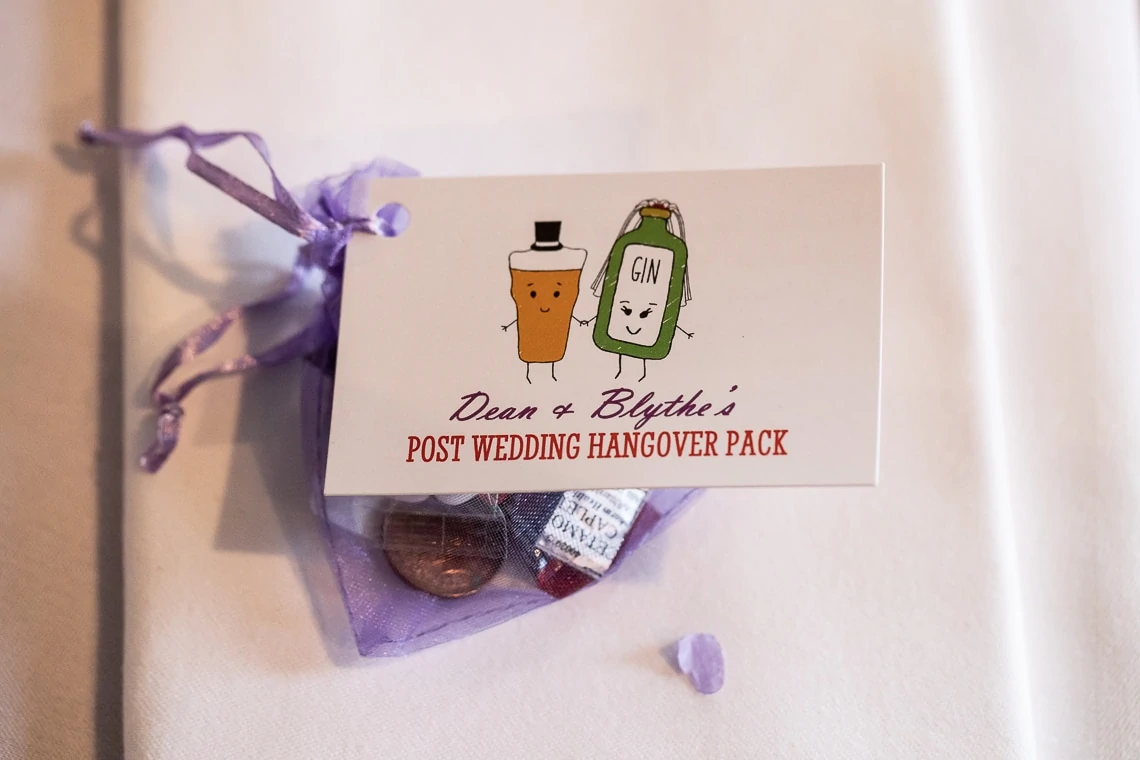 A post-wedding hangover pack with the label "dean & blythe's" featuring cartoon bottle and glass drawings, surrounded by candy in a purple mesh bag.