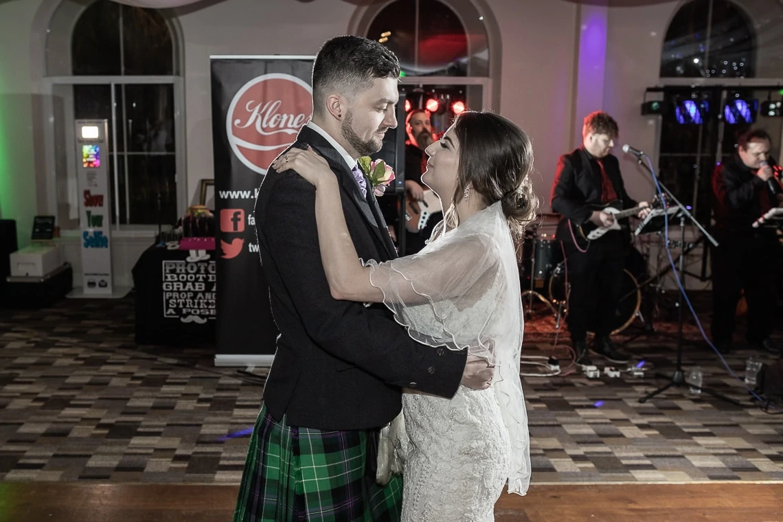 Bride and groom sharing a close dance at their wedding reception, with a band performing in the background and a patterned dance floor beneath them.