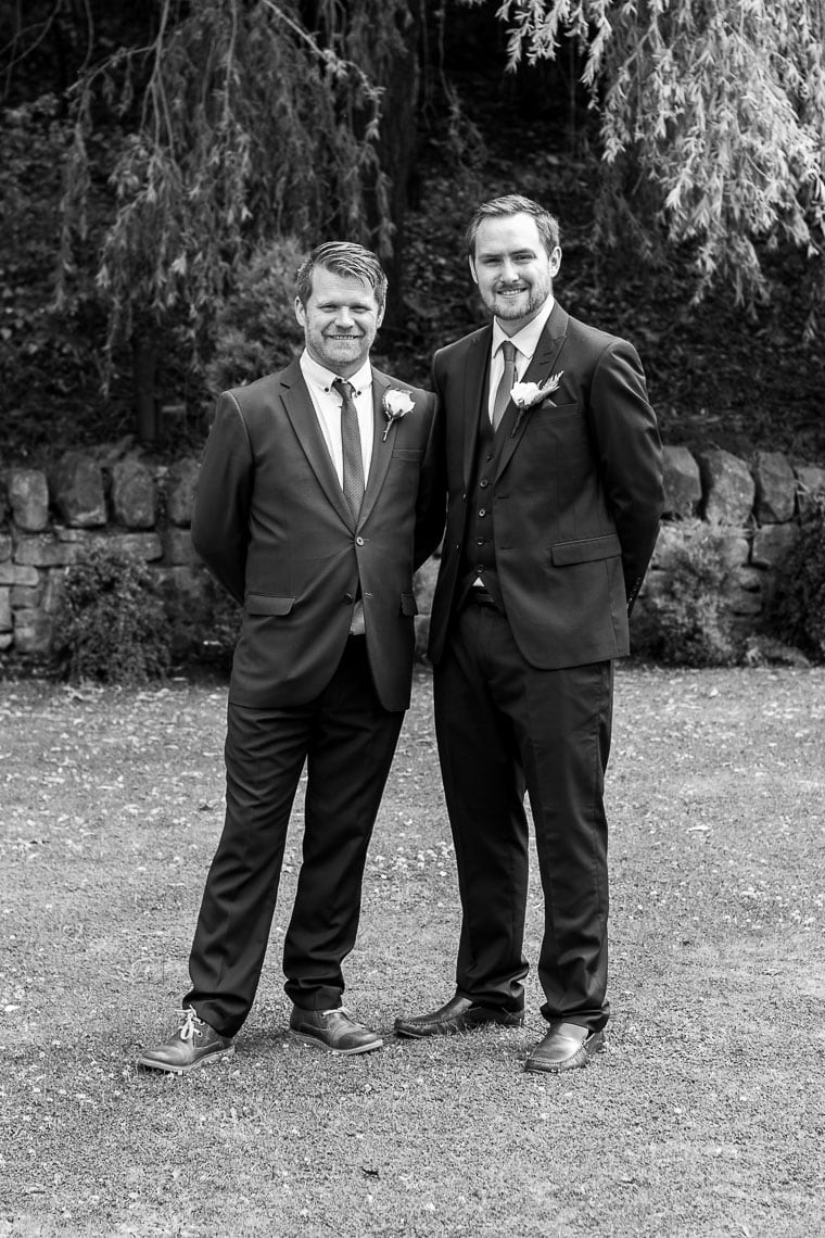 posed black and white photo of groom with bestman in garden outside wedding venue