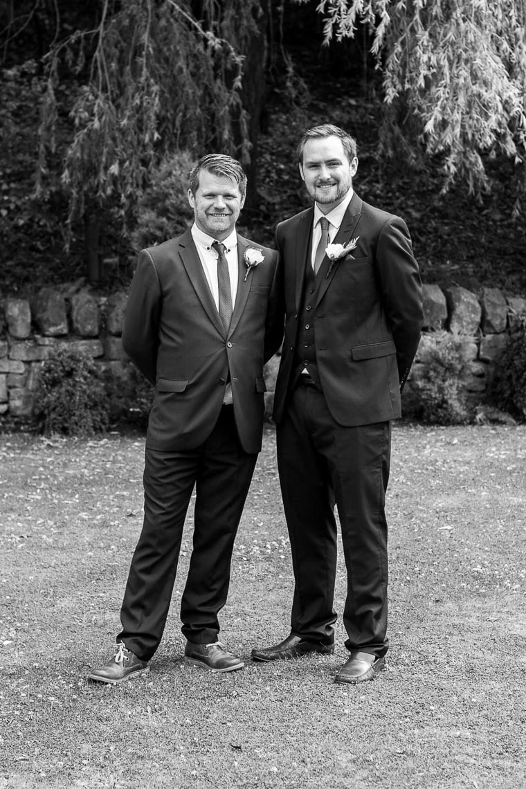 posed black and white photo of groom with bestman in garden outside wedding venue