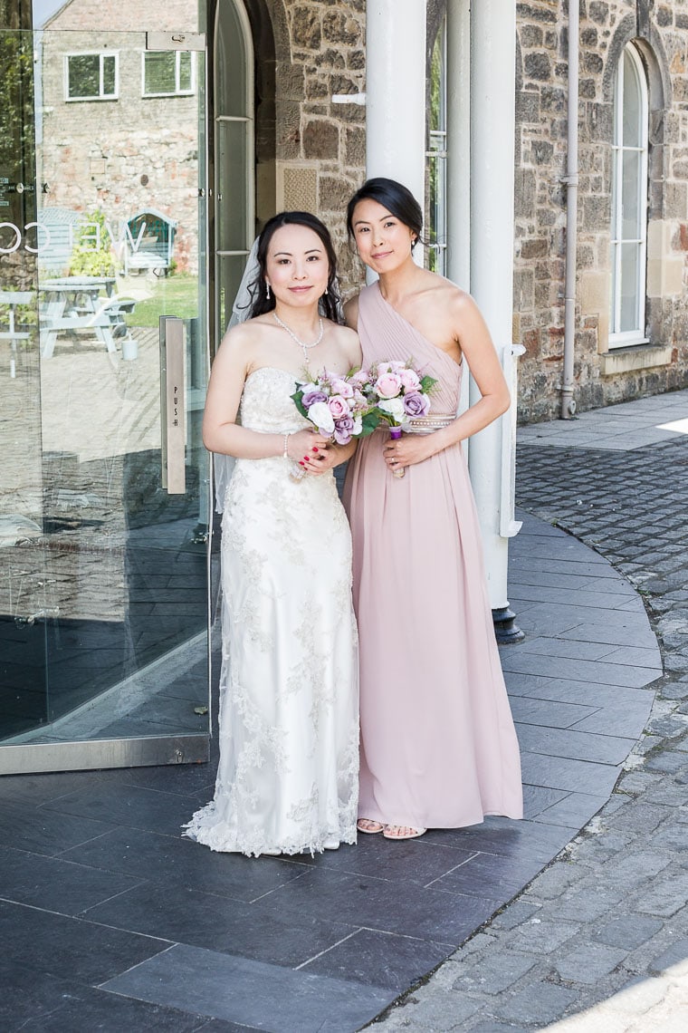 posed photo of bride with bridesmaid outside wedding venue entrance