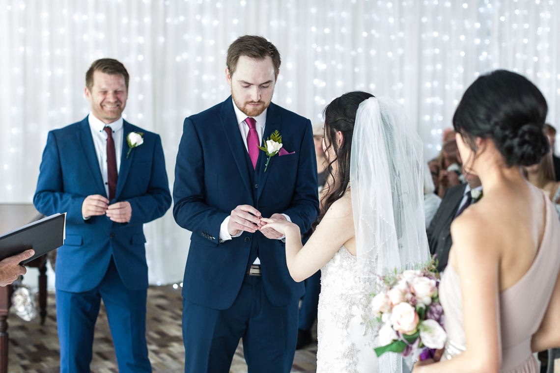 groom putting ring on bride's finger at wedding ceremony