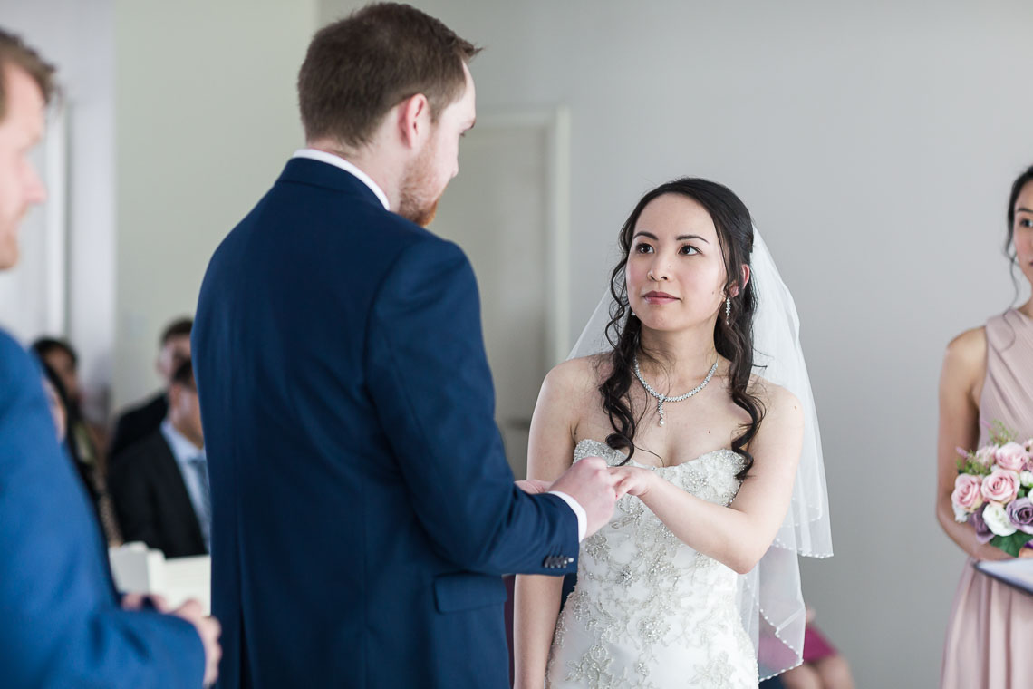 bride looking at groom as he places ring on her finger during wedding ceremony