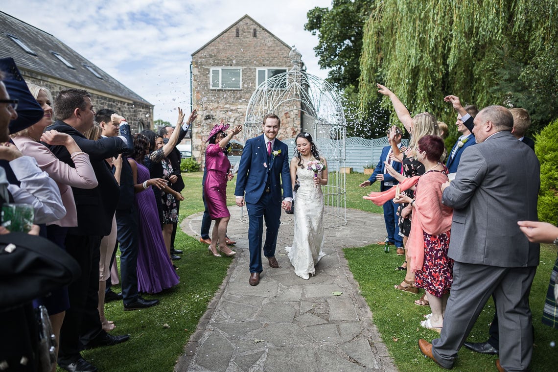 wedding guests throwing confetti at newlyweds outside in the garden