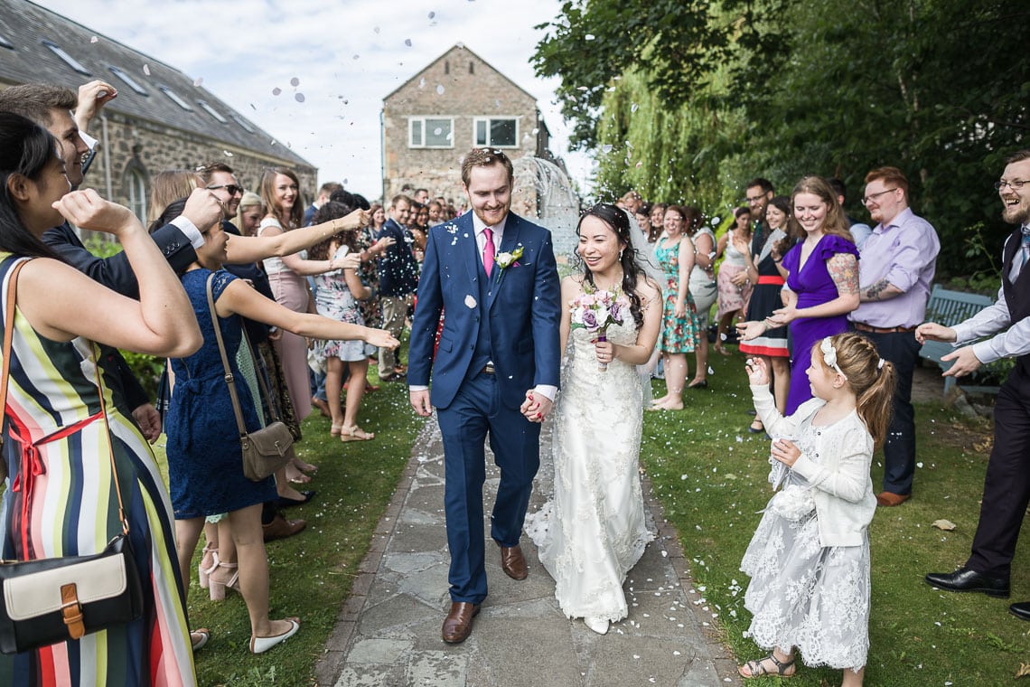 guests throw confetti at newlyweds in the garden