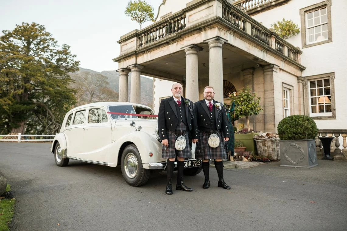 Exterior grooms at the entrance in front of their vintage car