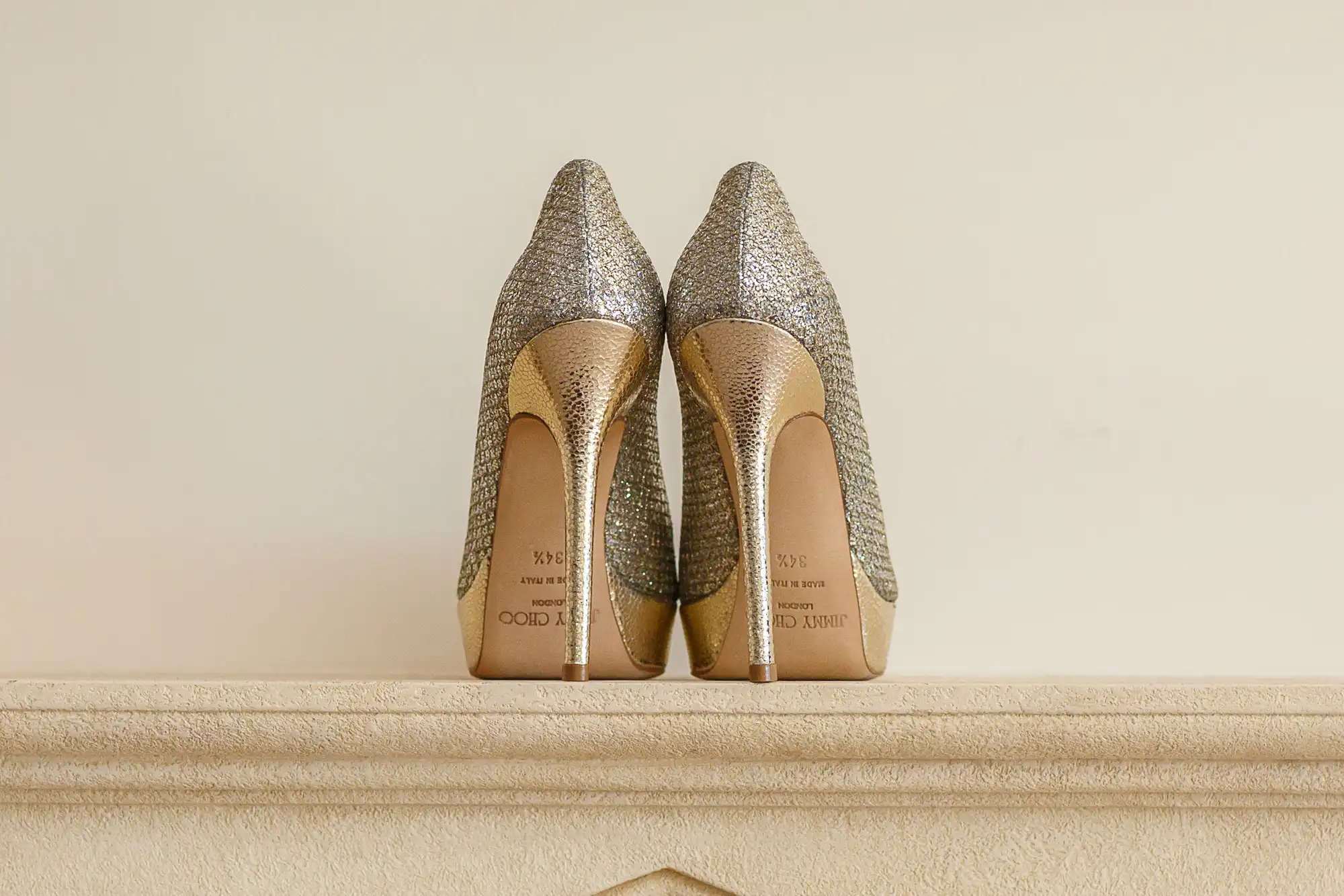 A pair of sparkly silver high-heeled shoes displayed on a neutral-colored shelf.