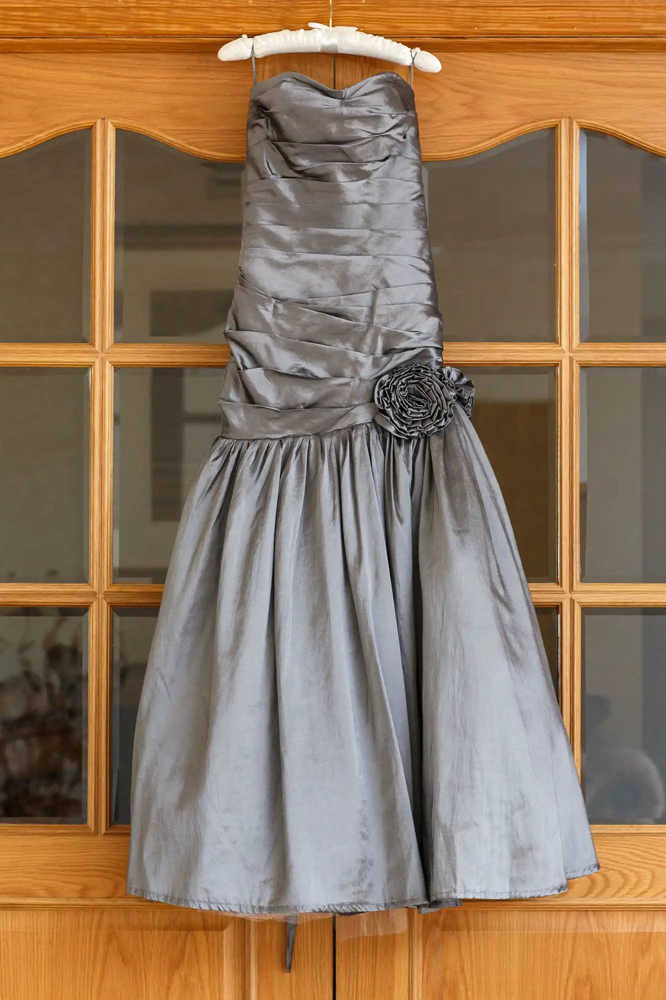 Gray cocktail dress with a rose detail, hanging on a wooden door with glass panels.