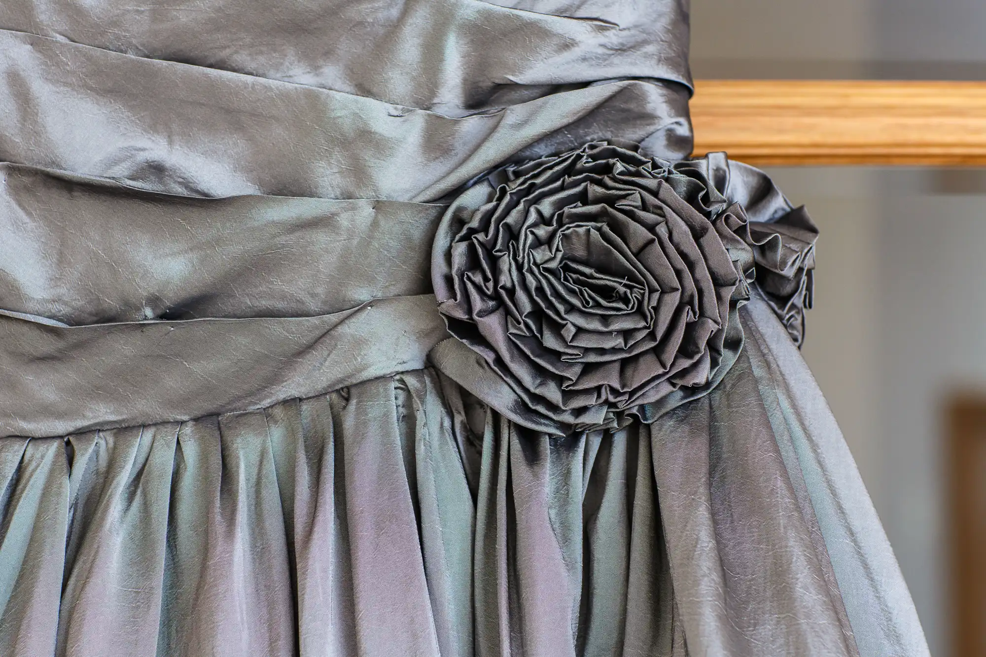 Close-up of a grey, ruched fabric dress with a large rosette detail on the waist and a pleated skirt.