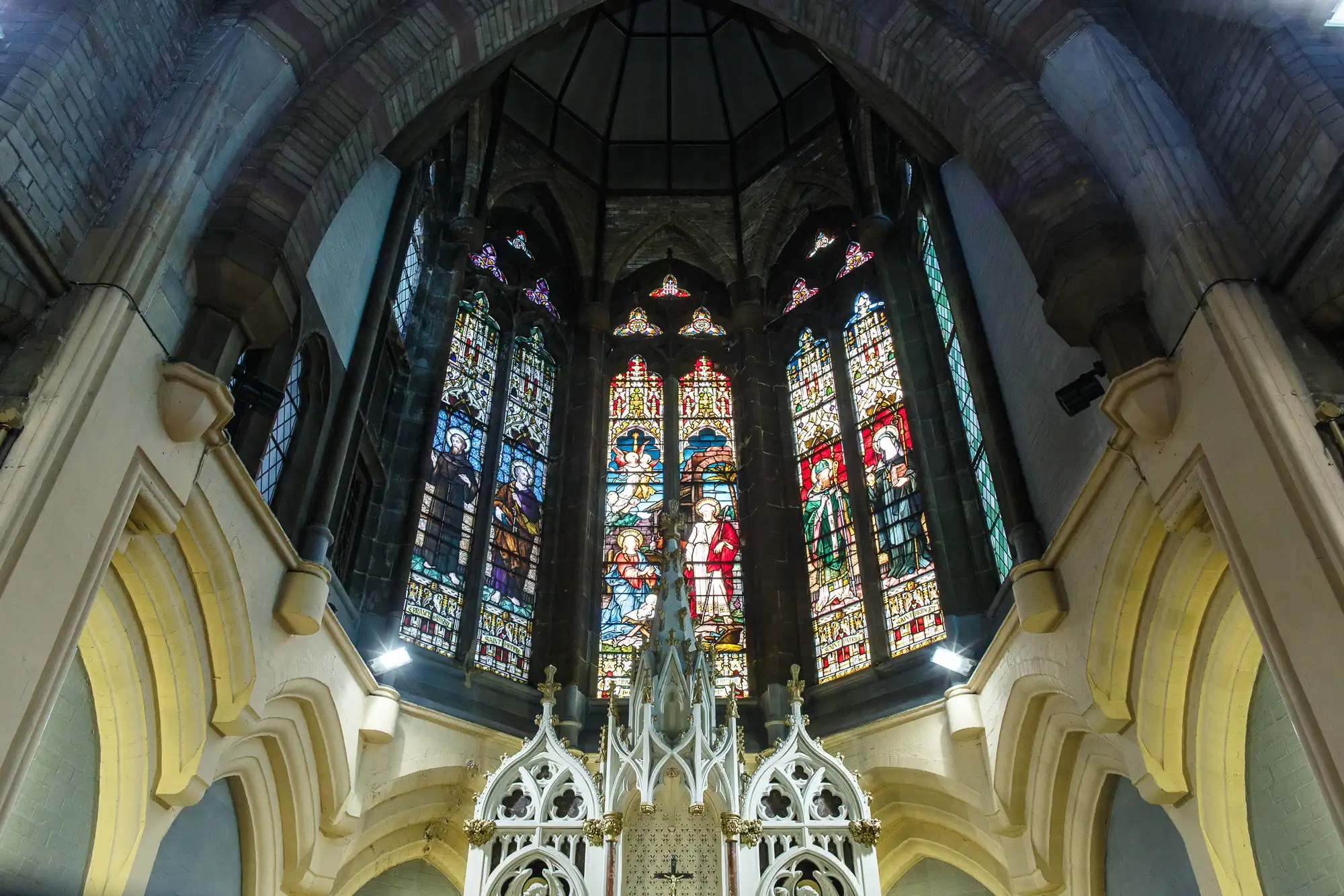 Interior of a gothic church showing ornate stained glass windows and elaborate stone arches.