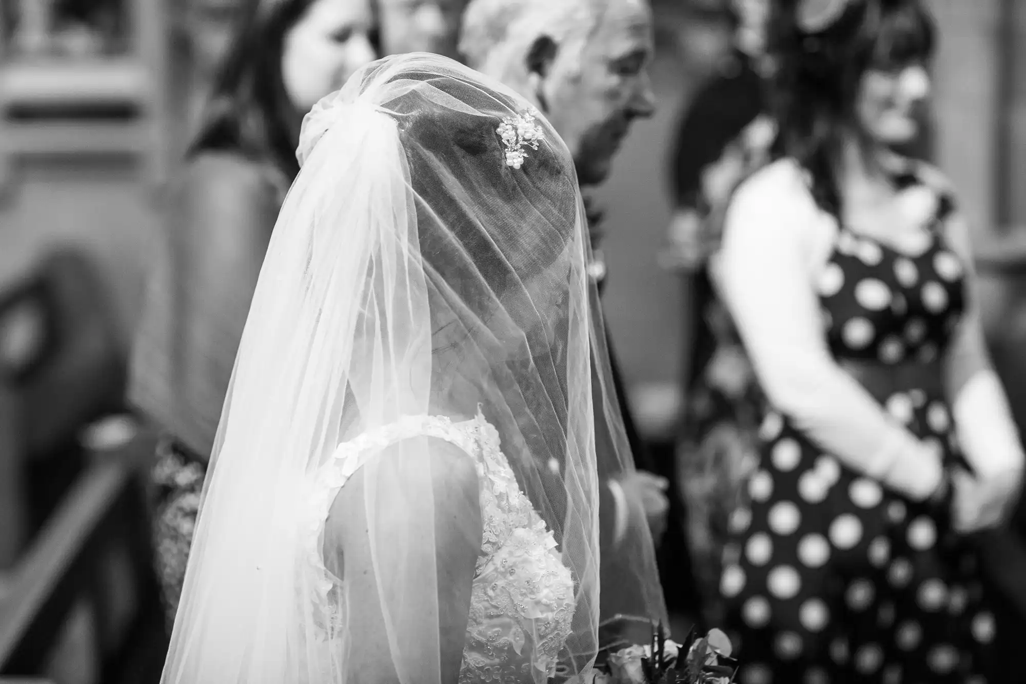 A bride wearing a veil and a wedding dress in a crowd of people at a wedding ceremony, picture in black and white.