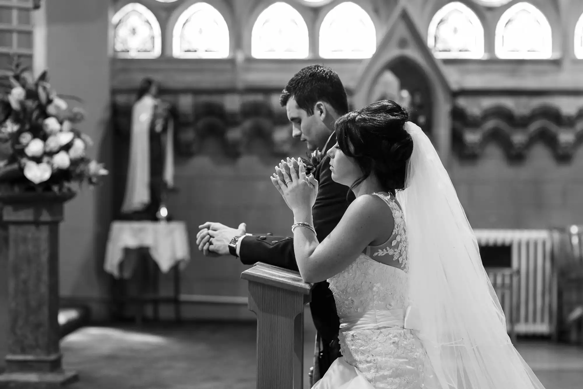 A bride and groom praying at the altar in a church, captured in black and white.