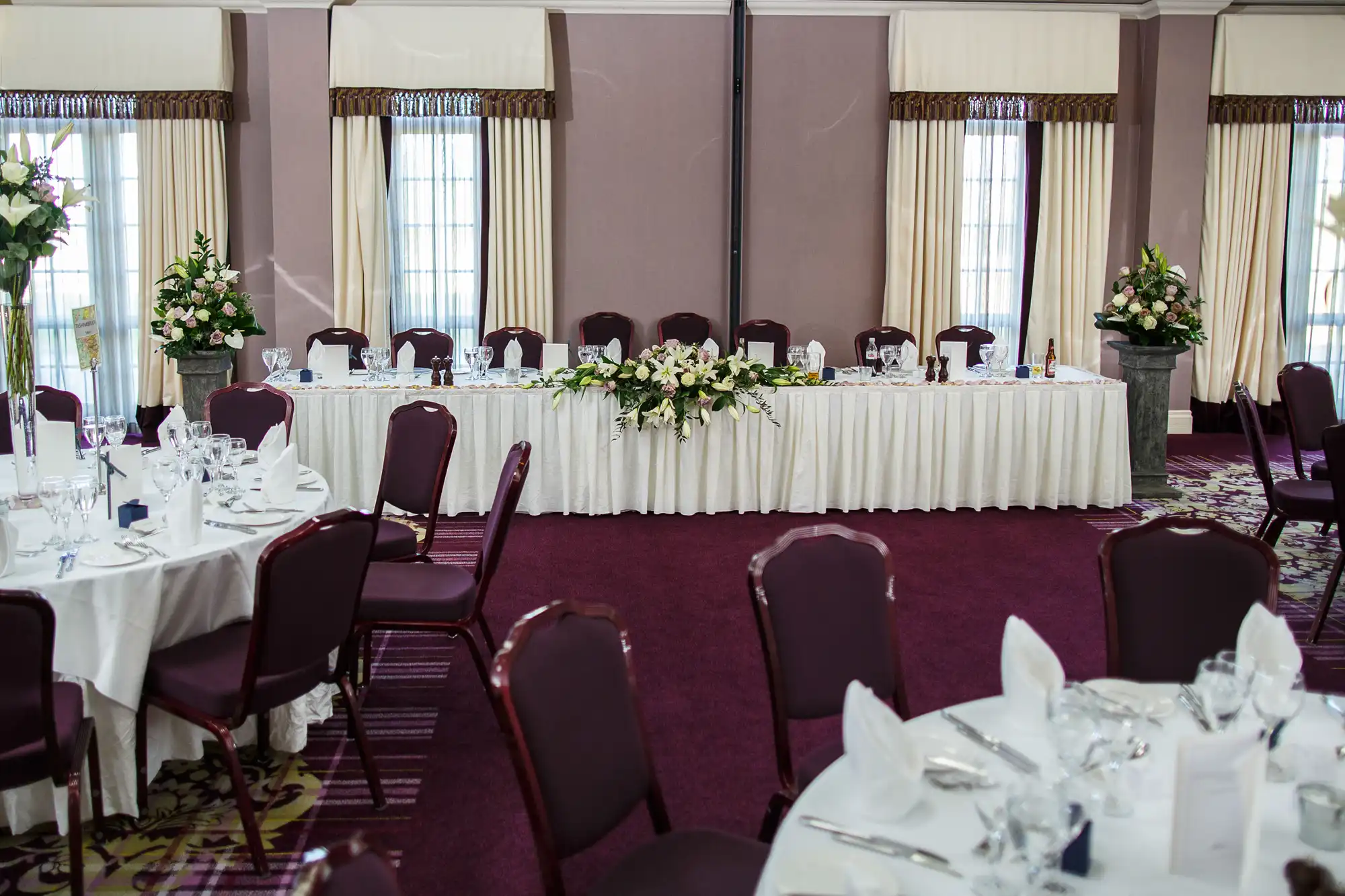 Elegant wedding reception room setup with decorated tables, floral centerpieces, and chairs arranged around a head table.