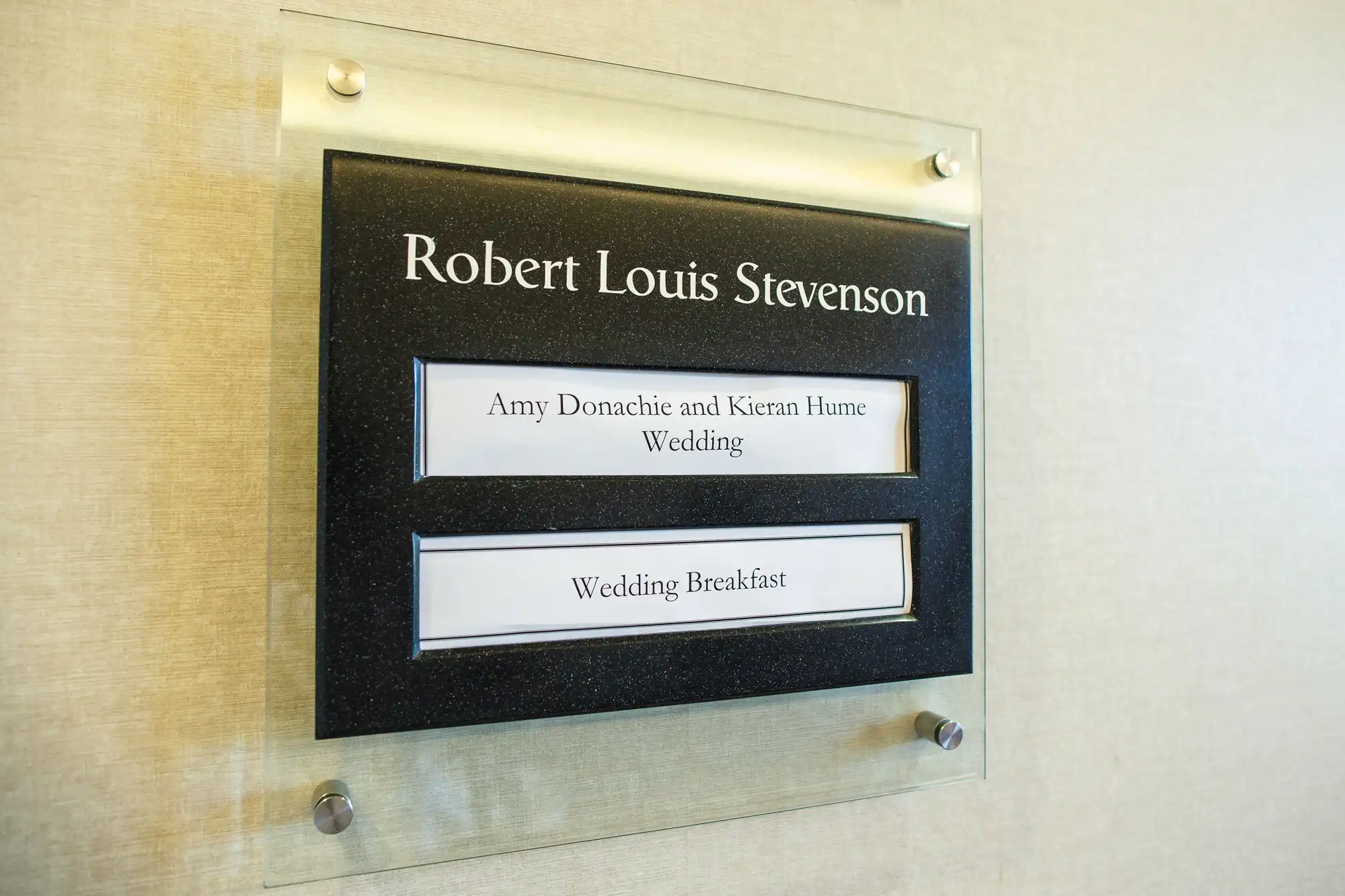 A plaque on a wall titled "robert louis stevenson" with subtext reading "amy donachie and kieran hume wedding" and "wedding breakfast" below.