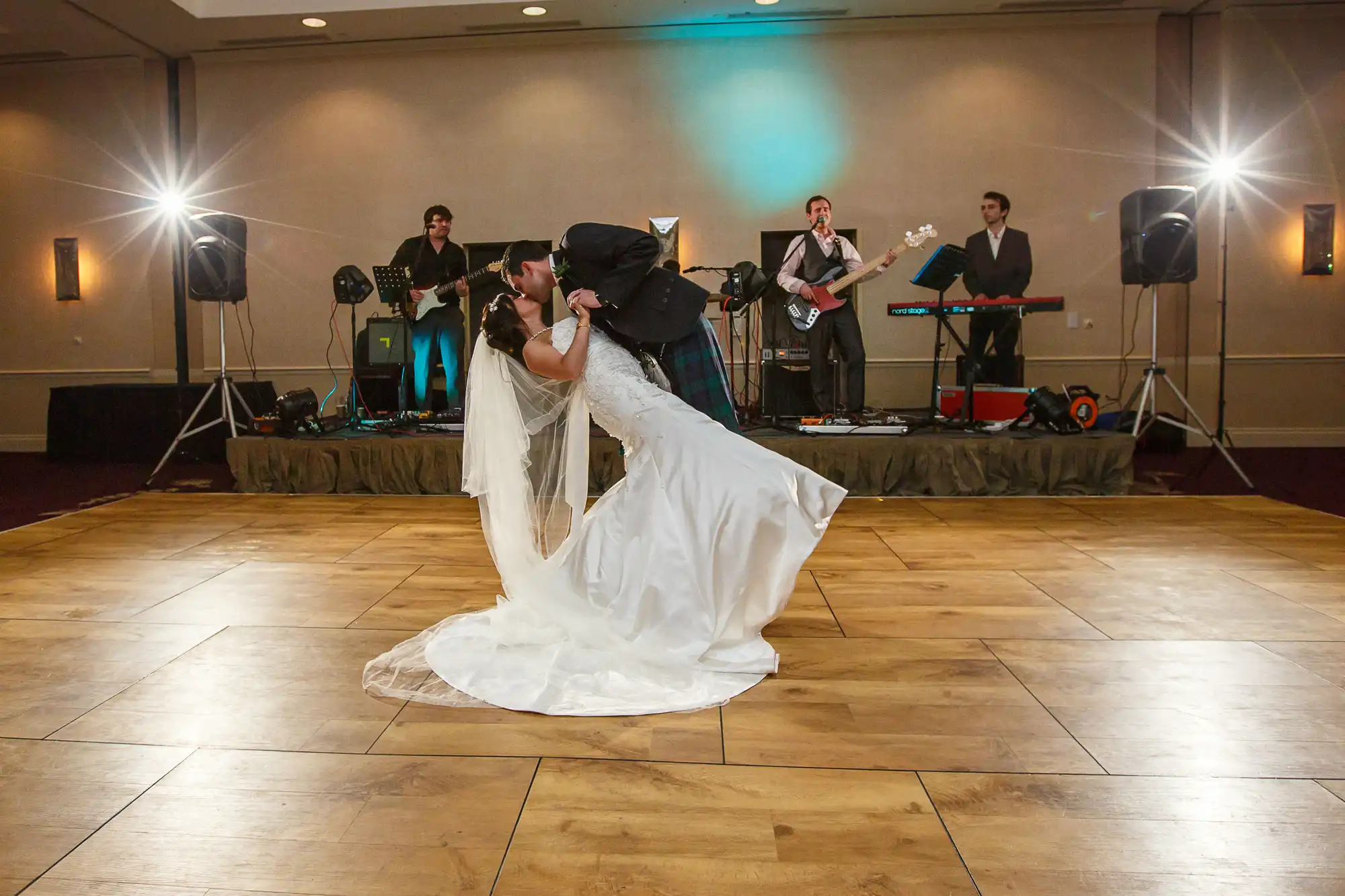 Bride and groom sharing a kiss on the dance floor while a band performs in the background at a wedding reception.