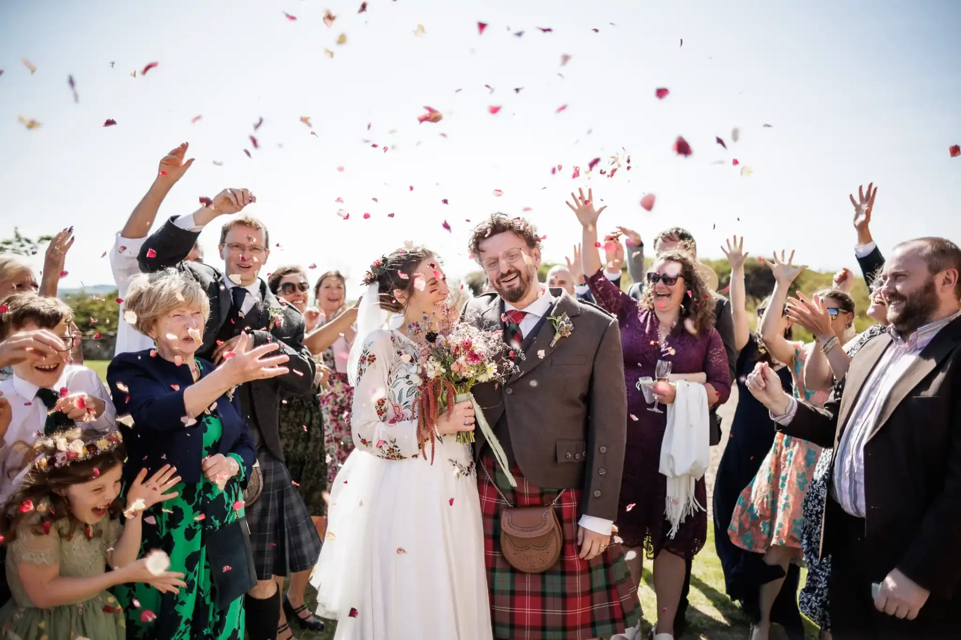 Fenton Tower wedding: A newlywed couple stands smiling as guests throw flower petals in celebration outdoors.