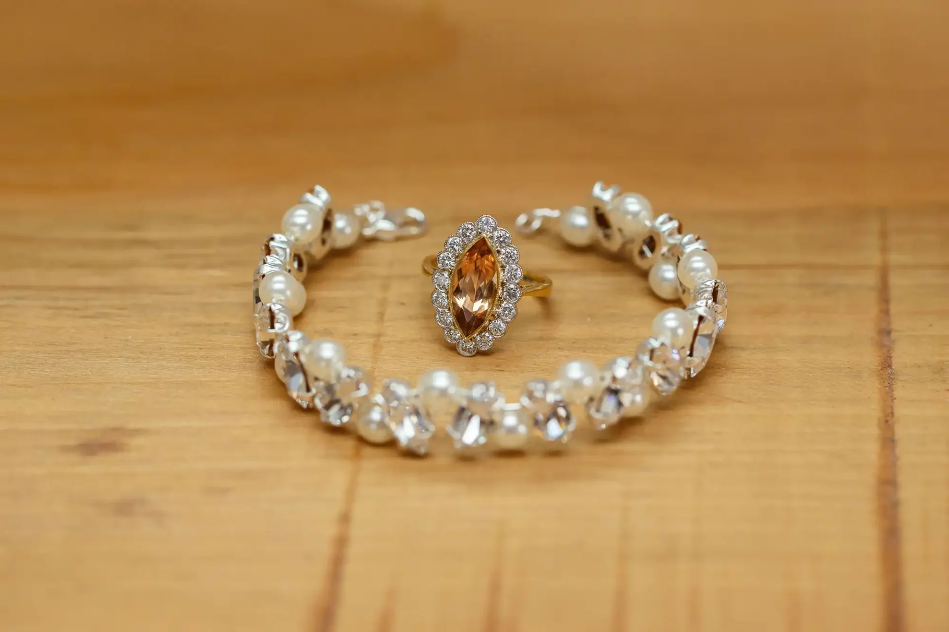 A pearl and crystal bracelet alongside a gold ring with an oval amber gemstone, displayed on a wooden surface.