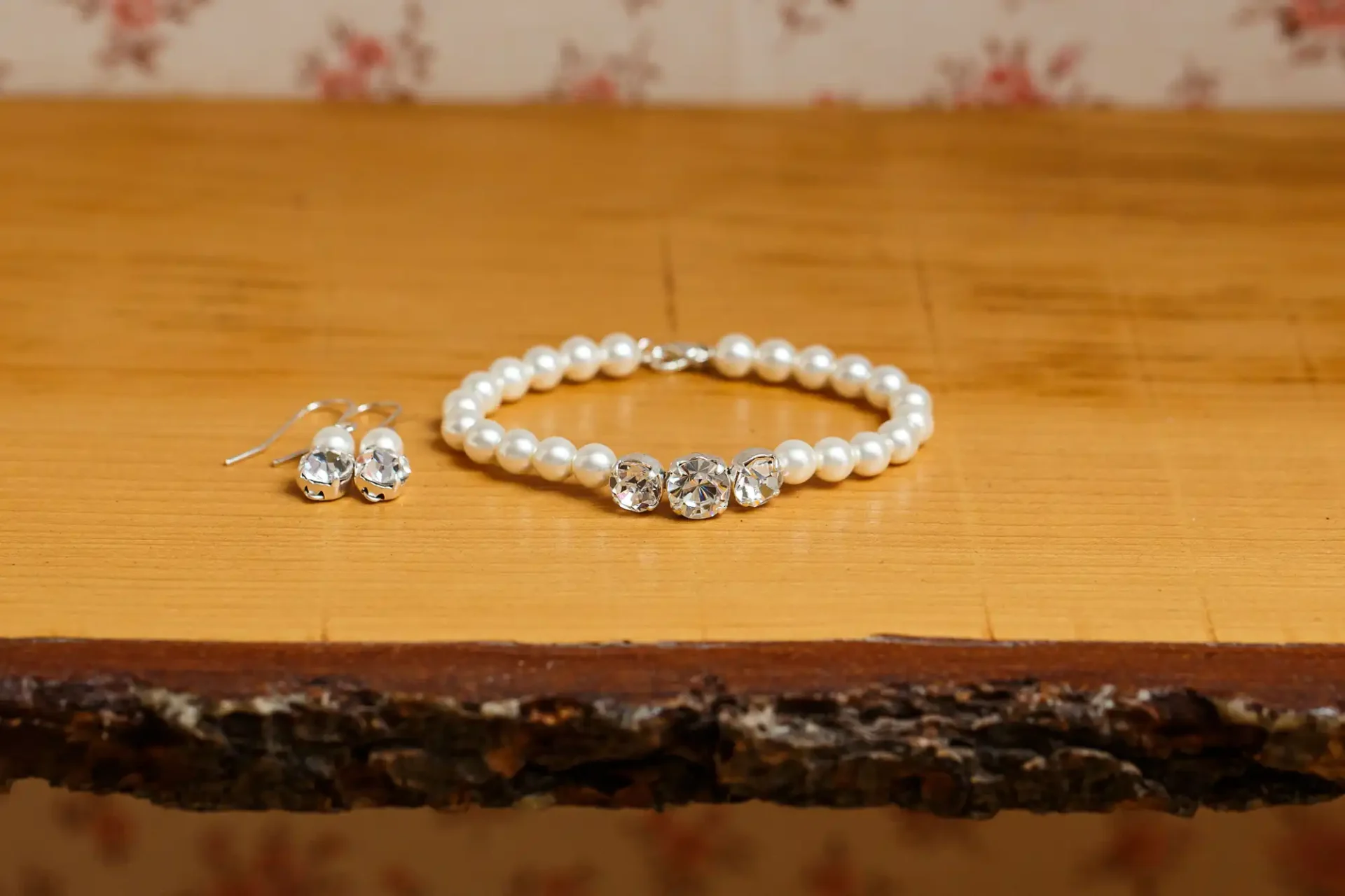Pearl bracelet and crystal earrings set on a wooden table with a rustic edge.