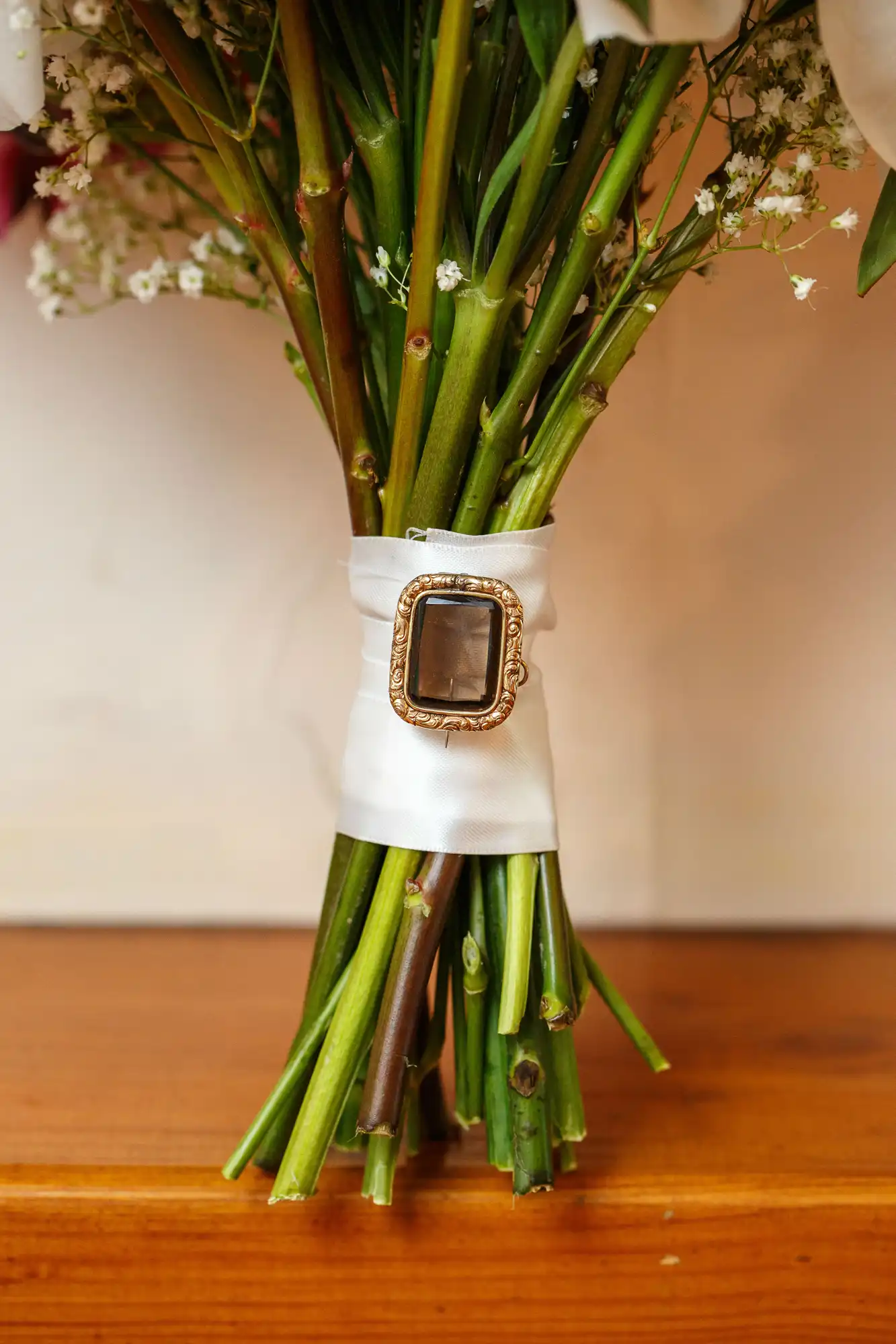 Bouquet of flowers tied with a white ribbon and embellished with a vintage cameo brooch, resting on a wooden surface.