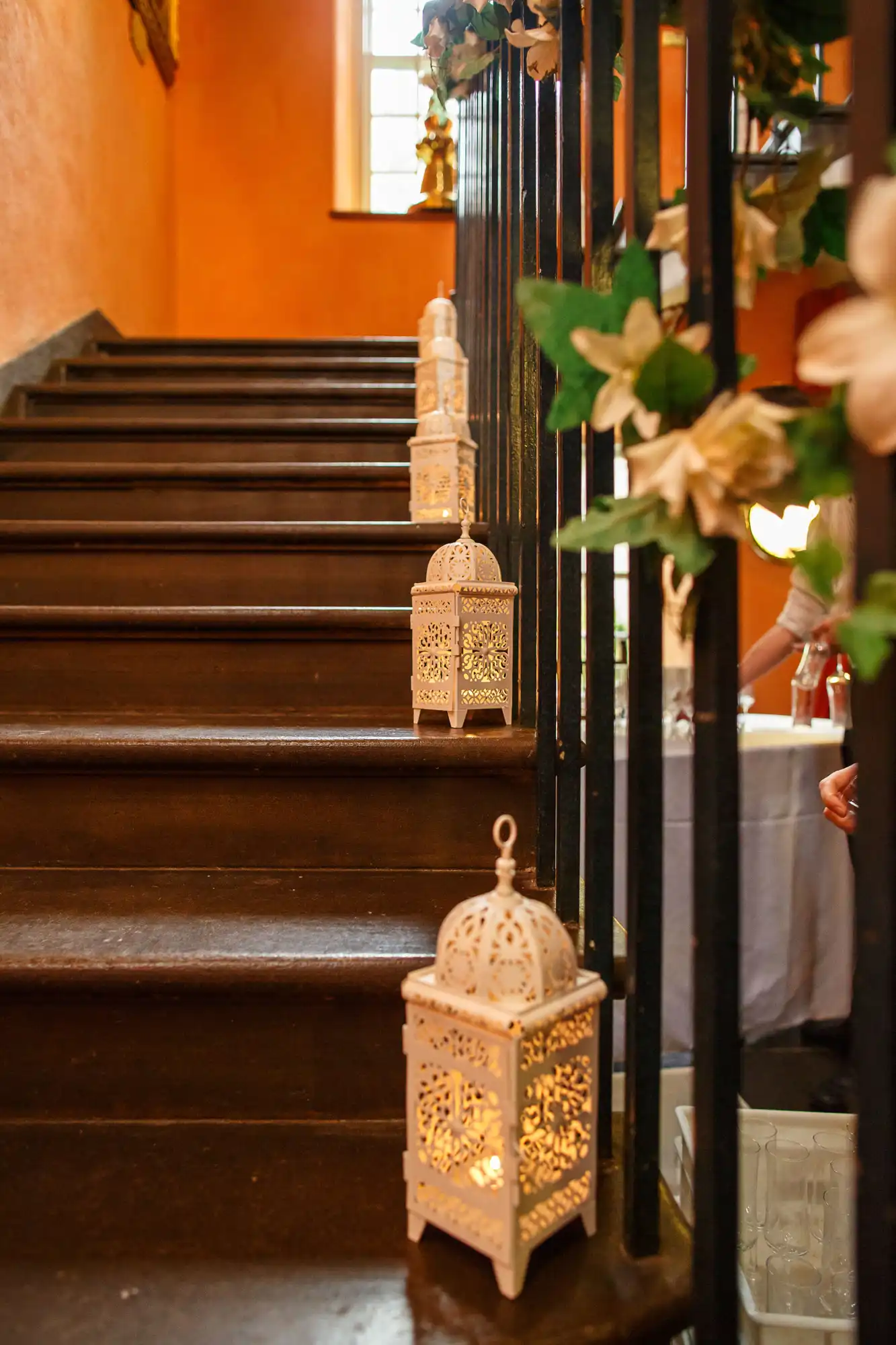 Decorative lanterns on wooden stair steps in a warmly lit indoor setting, with partial view of a railing and floral decor.