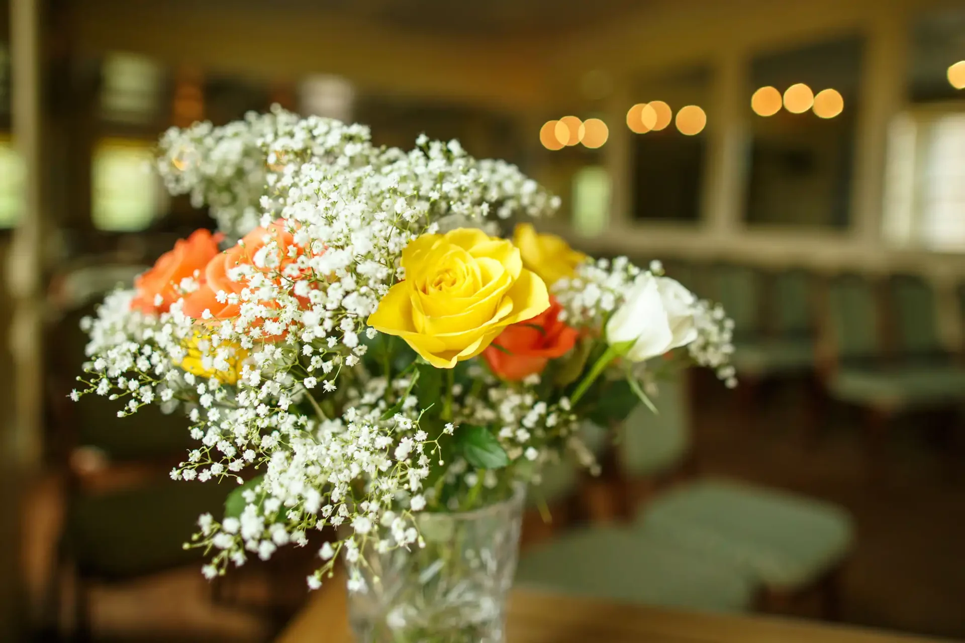 A vibrant bouquet of roses with mixed colors complemented by baby's breath, displayed in a vase with a softly blurred restaurant background.