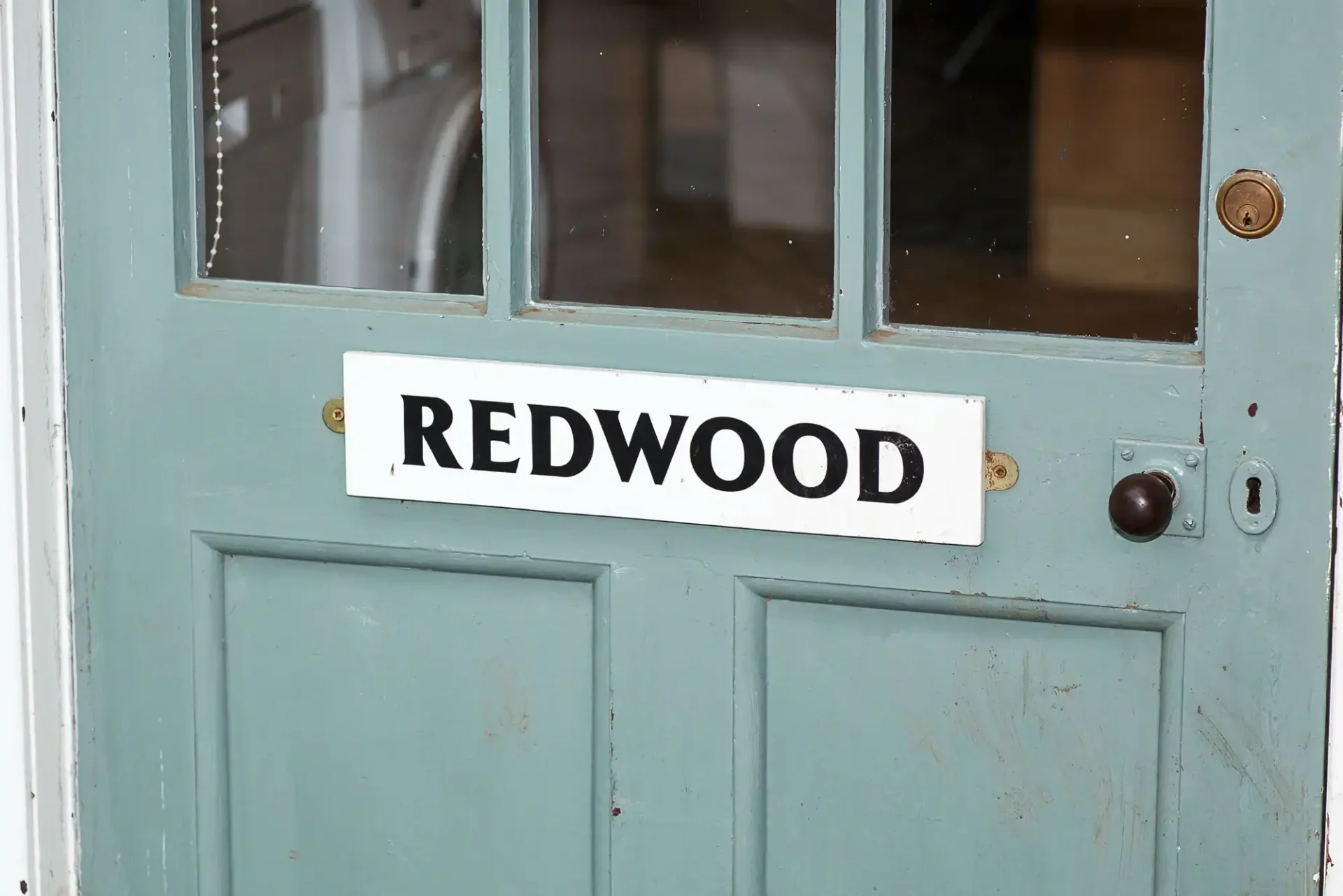 Close-up view of a worn teal door with a white sign that reads "redwood" affixed to its glass window.