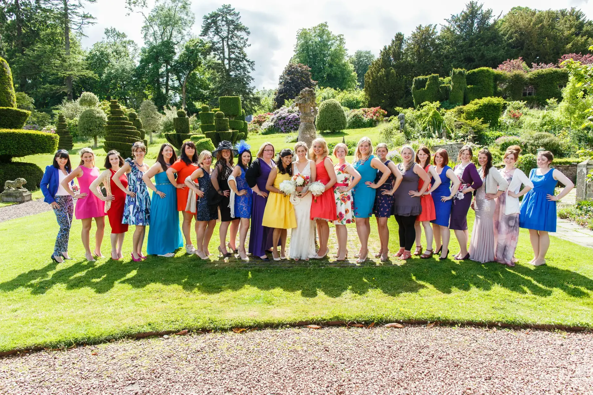 Group of women in colorful dresses posing for a photo at a garden party on a sunny day.