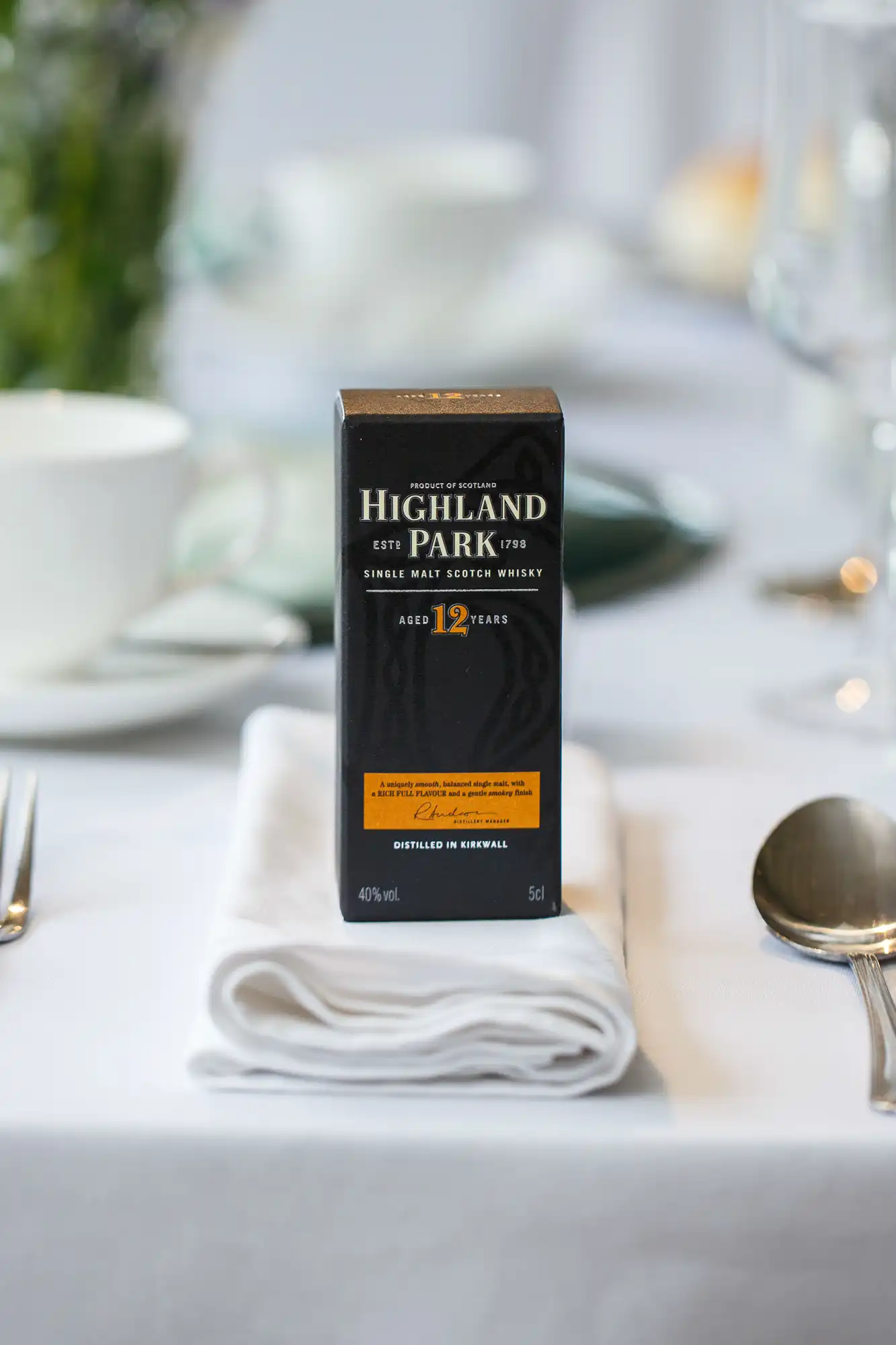 A bottle of highland park 12-year-old single malt scotch whisky on a dining table, set with white linen and silverware.
