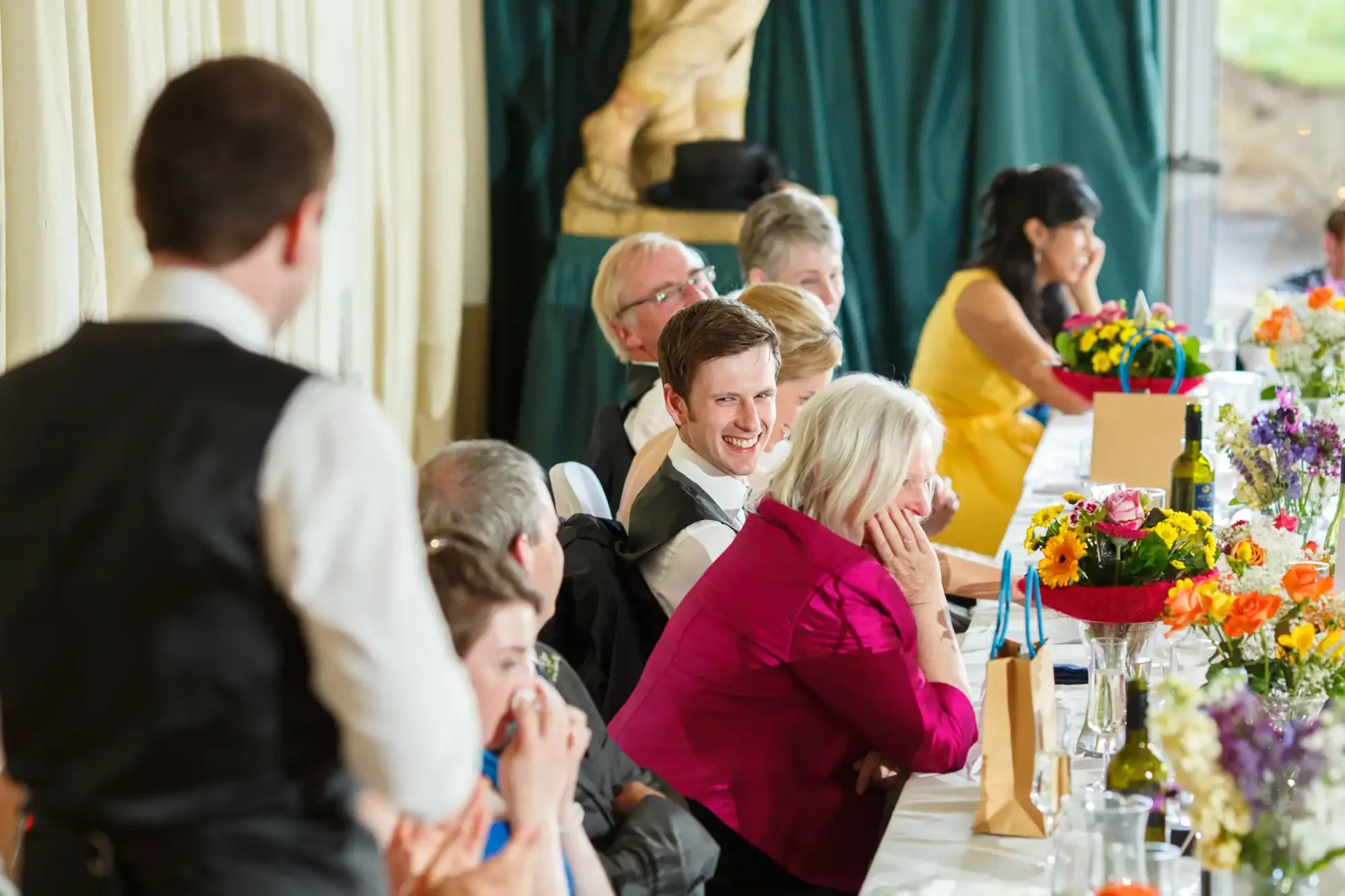 Guests enjoying conversation at a lively wedding reception table decorated with colorful flowers.