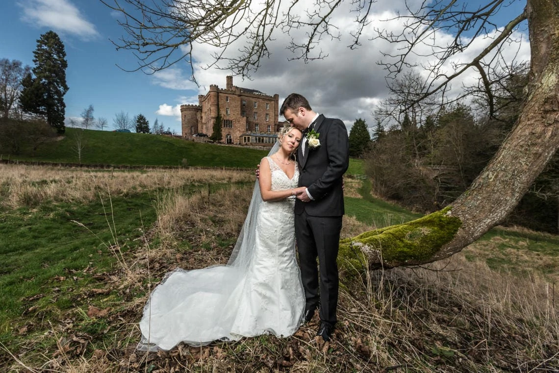 Gardens - newlyweds embrace in the valley with castle in the background